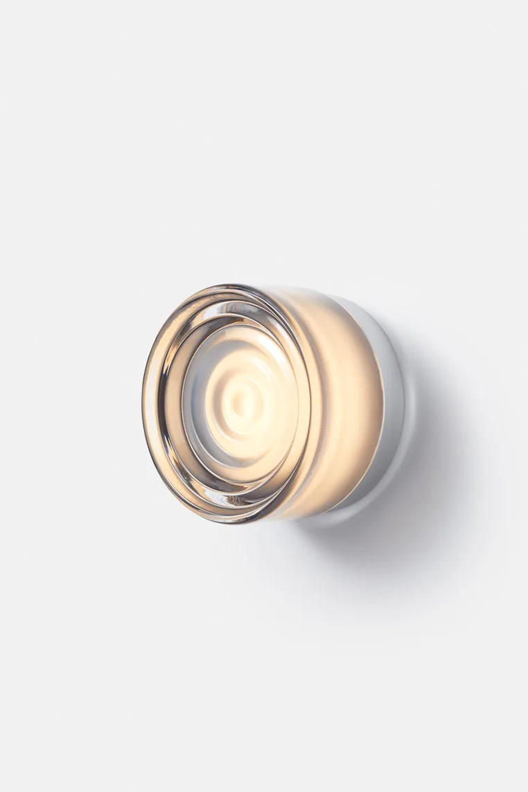 Minimalist wall-mounted light fixture with warm brass and frosted glass elements casting soft ambient light, by Theo Richardson.