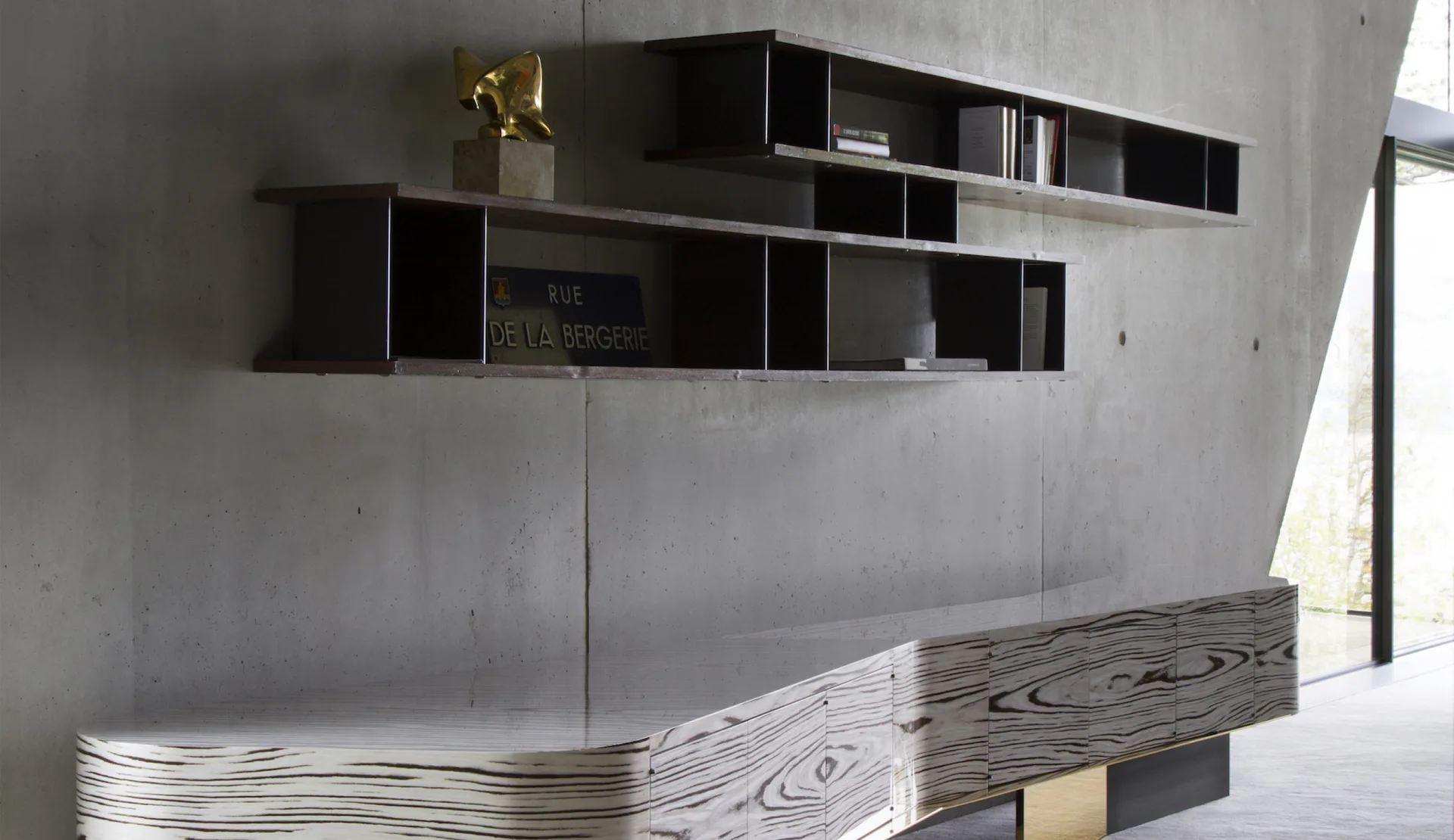 Modern minimalist interior with black floating shelving units and a curved wood-grain reception desk in a bright white space by Thierry Lemaire.