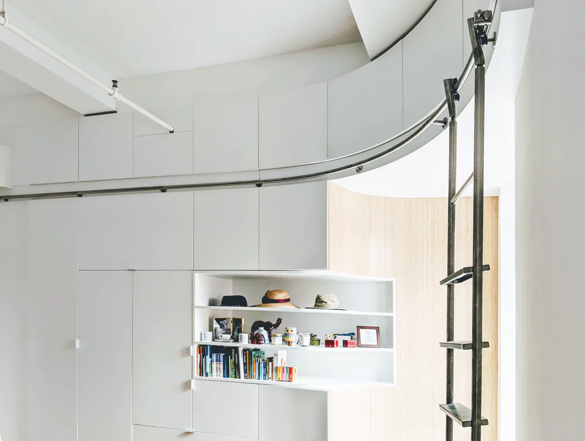 Minimalist white interior with curved track lighting, built-in shelving displaying books and objects, and geometric wall paneling by Thomas Diorio.