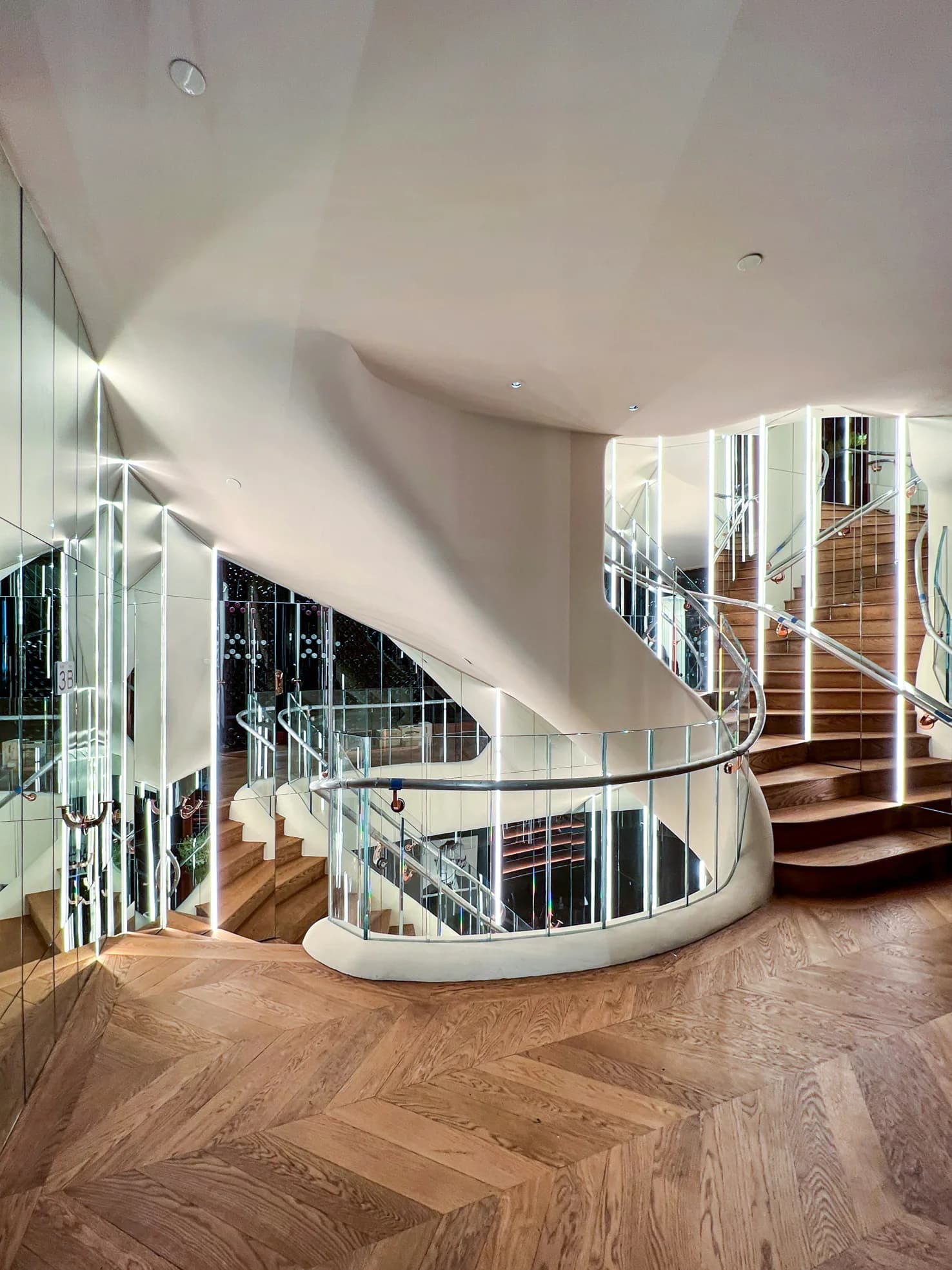 Modern spiral staircase with white curved walls, glass railings, and wooden steps in a bright multi-level interior by Thomas Diorio.
