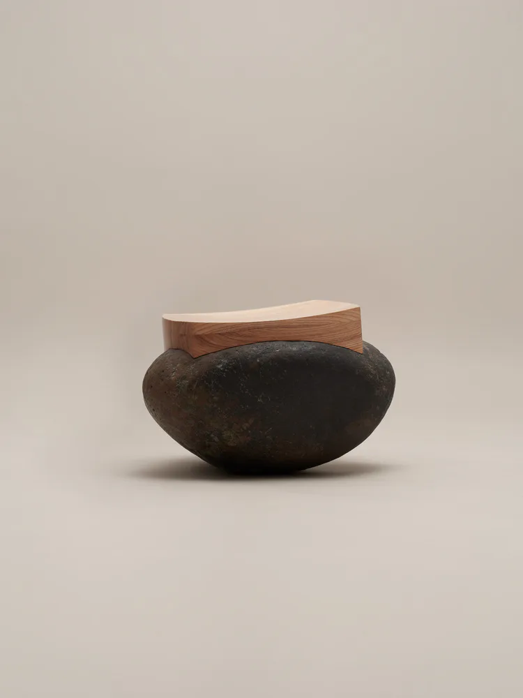 Dark ceramic bowl with organic, rounded form topped with a light wood rim element, photographed against a neutral background by Thomas Yang.