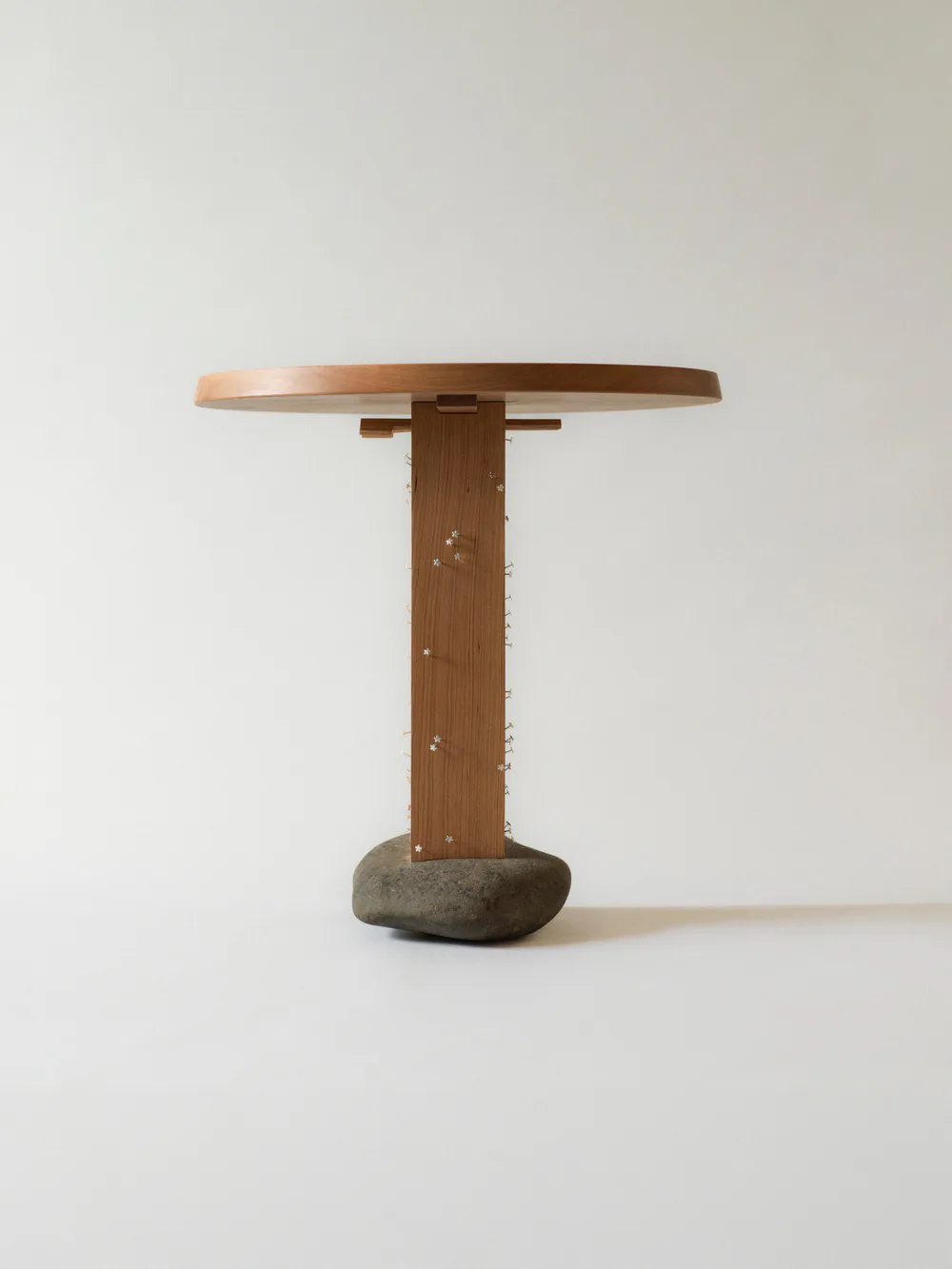 Sculptural side table with wooden stem, concrete base, and curved wood top shot against white background by Thomas Yang.