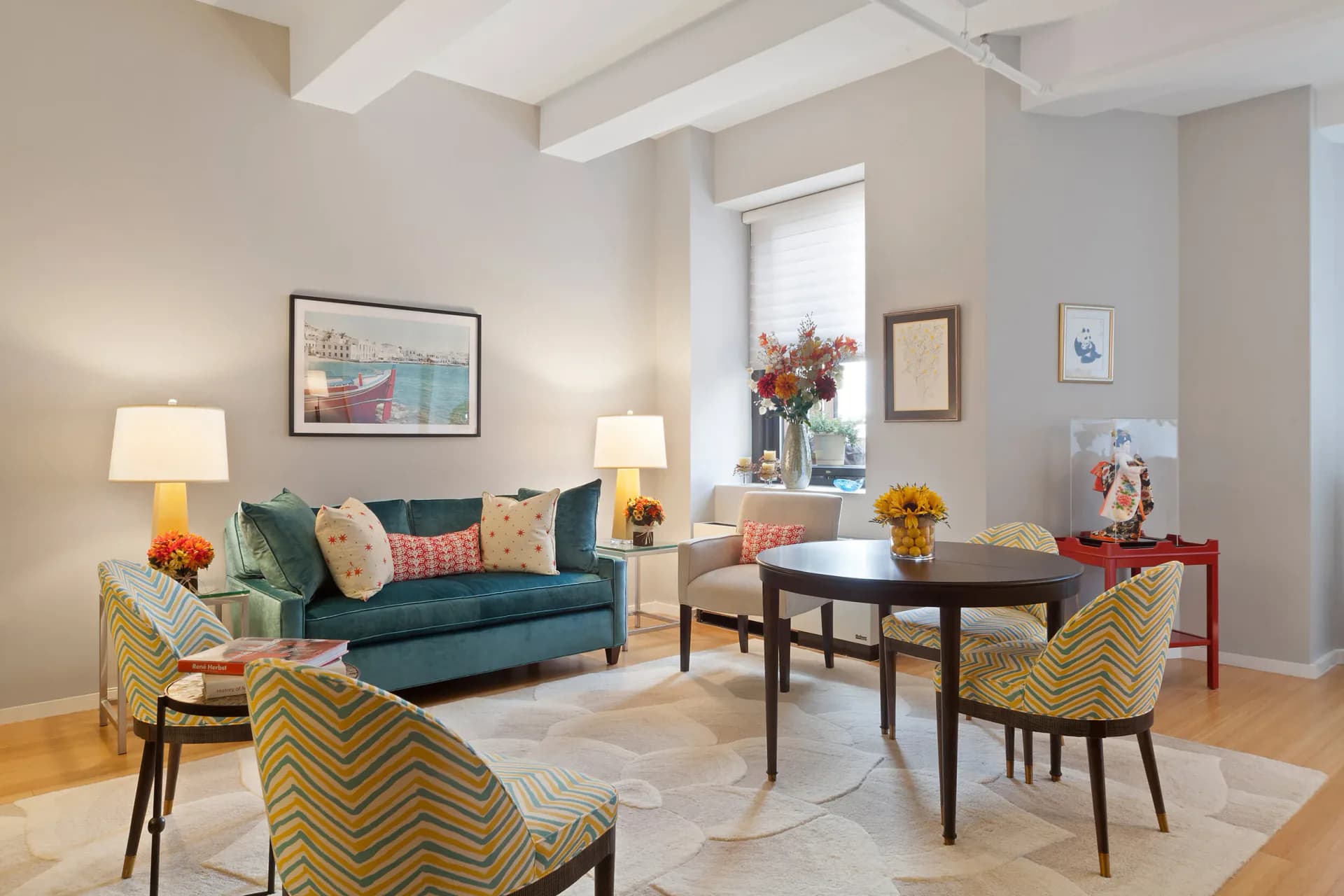 Modern living room with dark blue sofa, mustard chevron chairs, black dining table, and warm neutral palette with exposed beams by Tiffany Hicks.