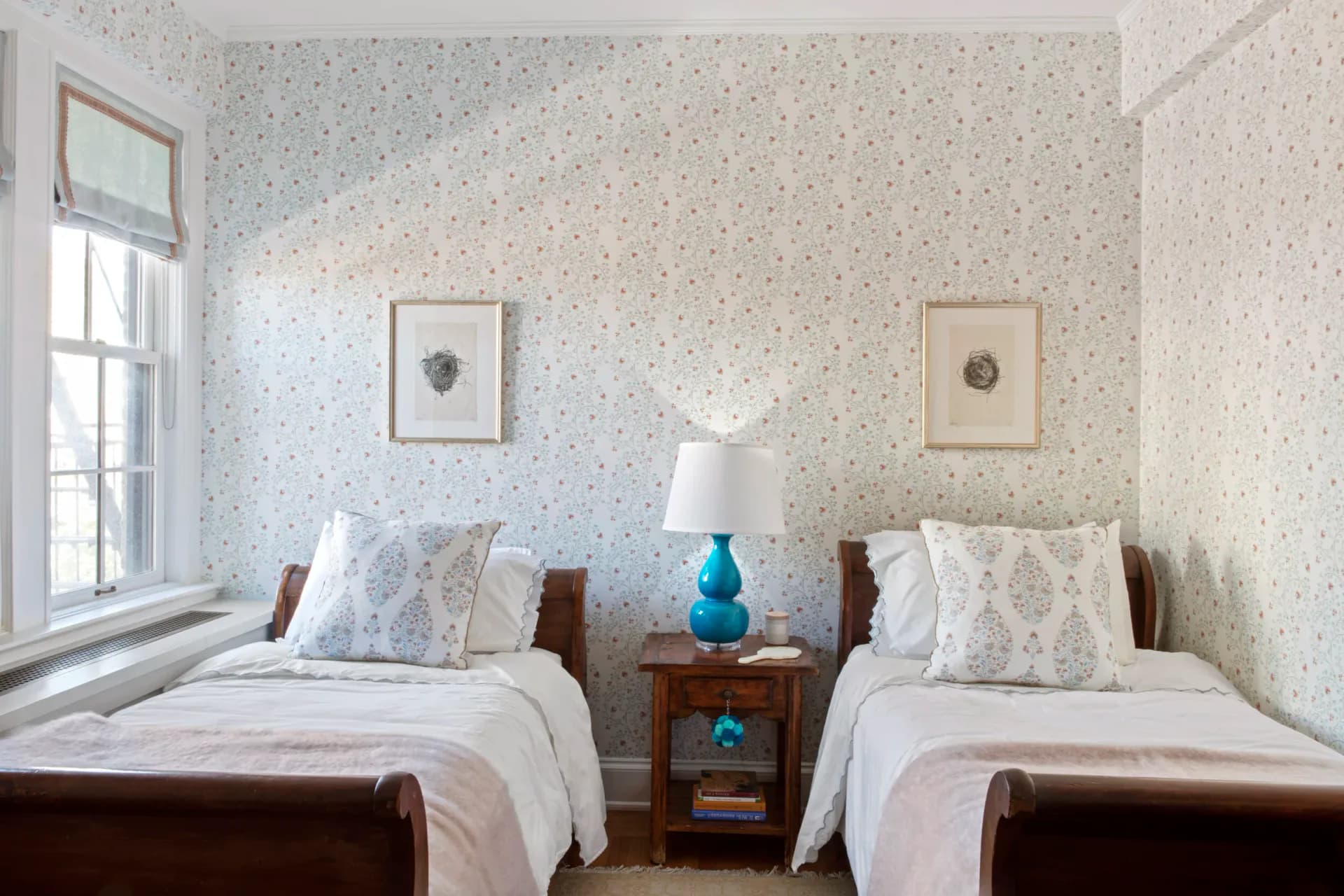 Twin bedroom with floral wallpaper, dark wood beds, shared nightstand, and framed botanical prints by Tiffany Hicks.