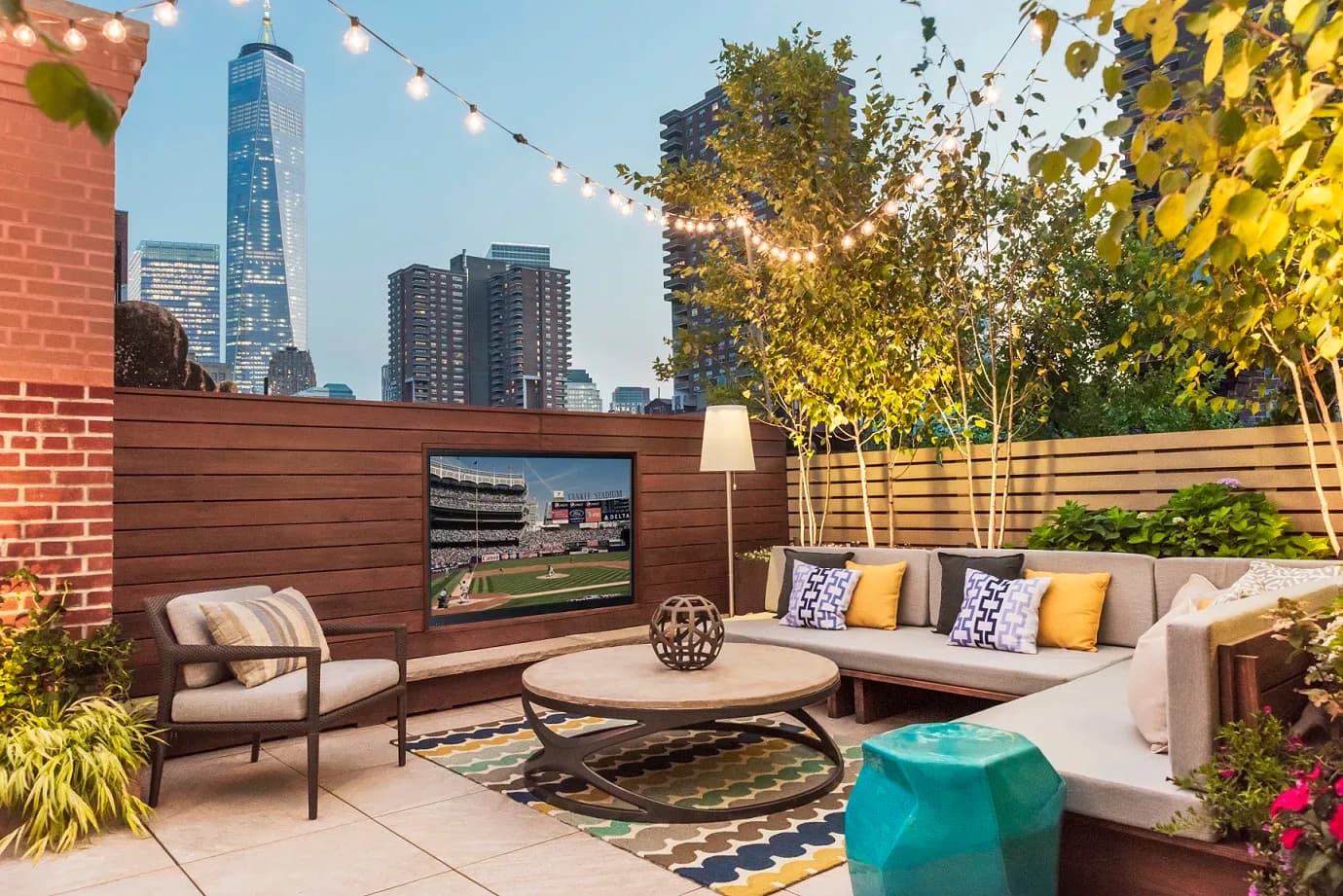 Rooftop terrace with modern seating, wooden privacy screens, outdoor TV, decorative pillows, and city skyline views by Tillie O'Reilly.
