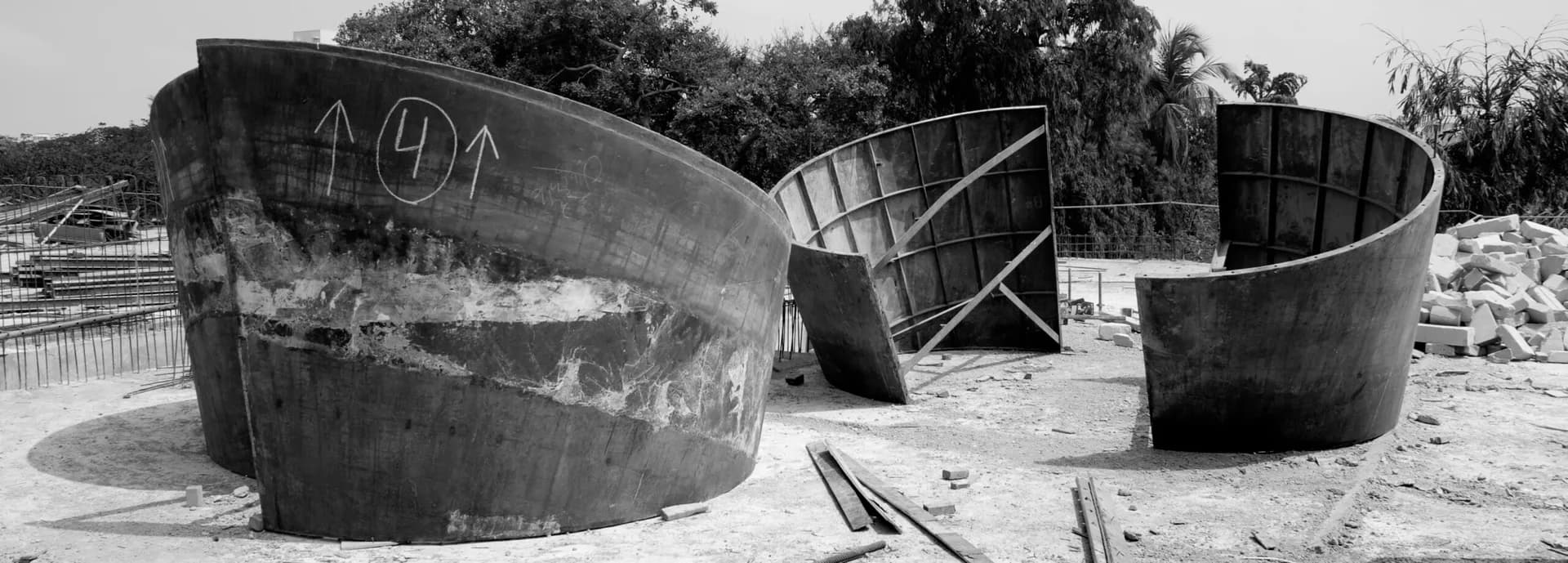 Weathered industrial concrete cylindrical vessels arranged in sandy landscape with vegetation, monochromatic architectural photography by Tod Williams.