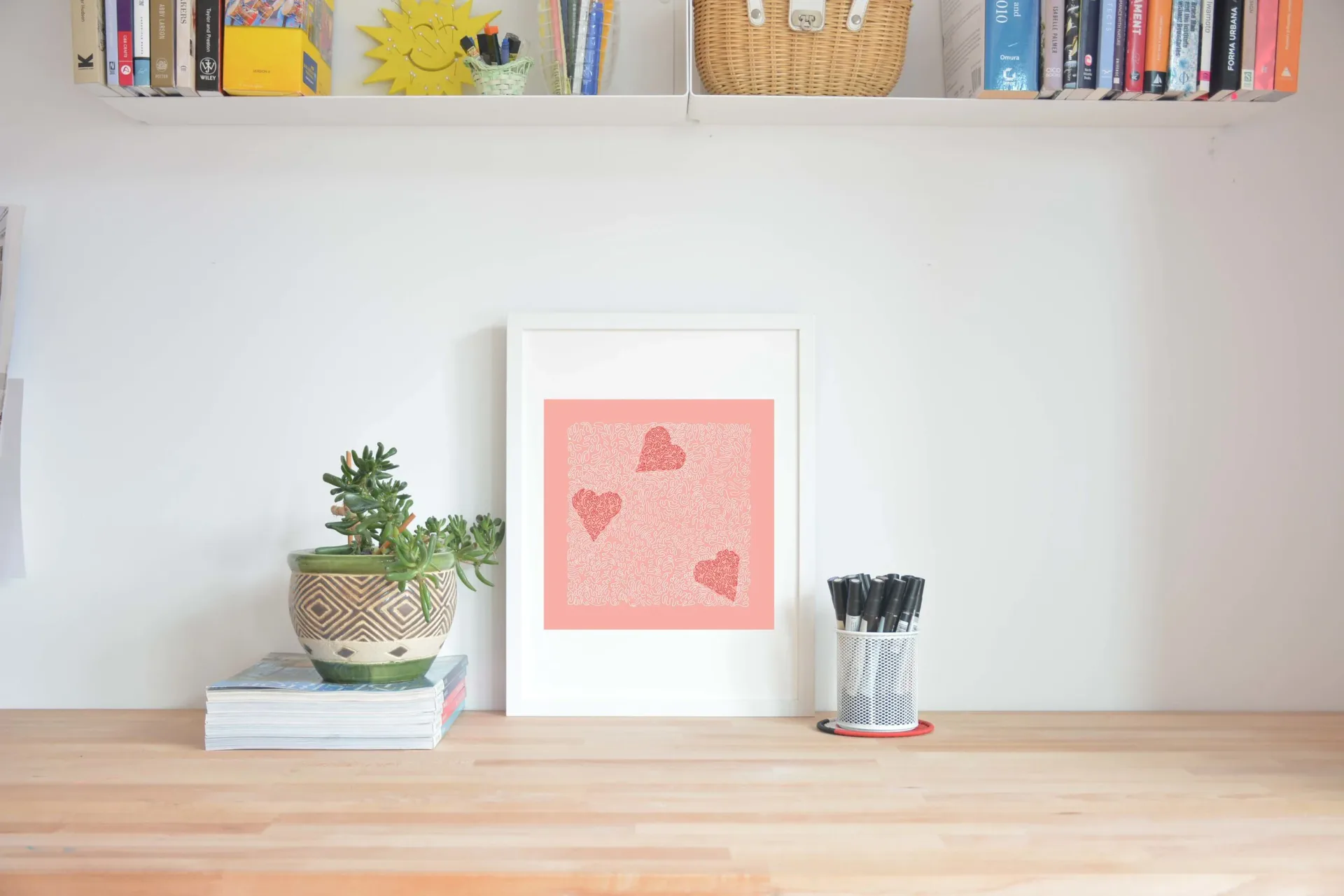 Styled wooden desk workspace featuring a potted succulent, stacked books, framed pink heart artwork, and brush holder, designed by Tolu Odunfa Dragone.