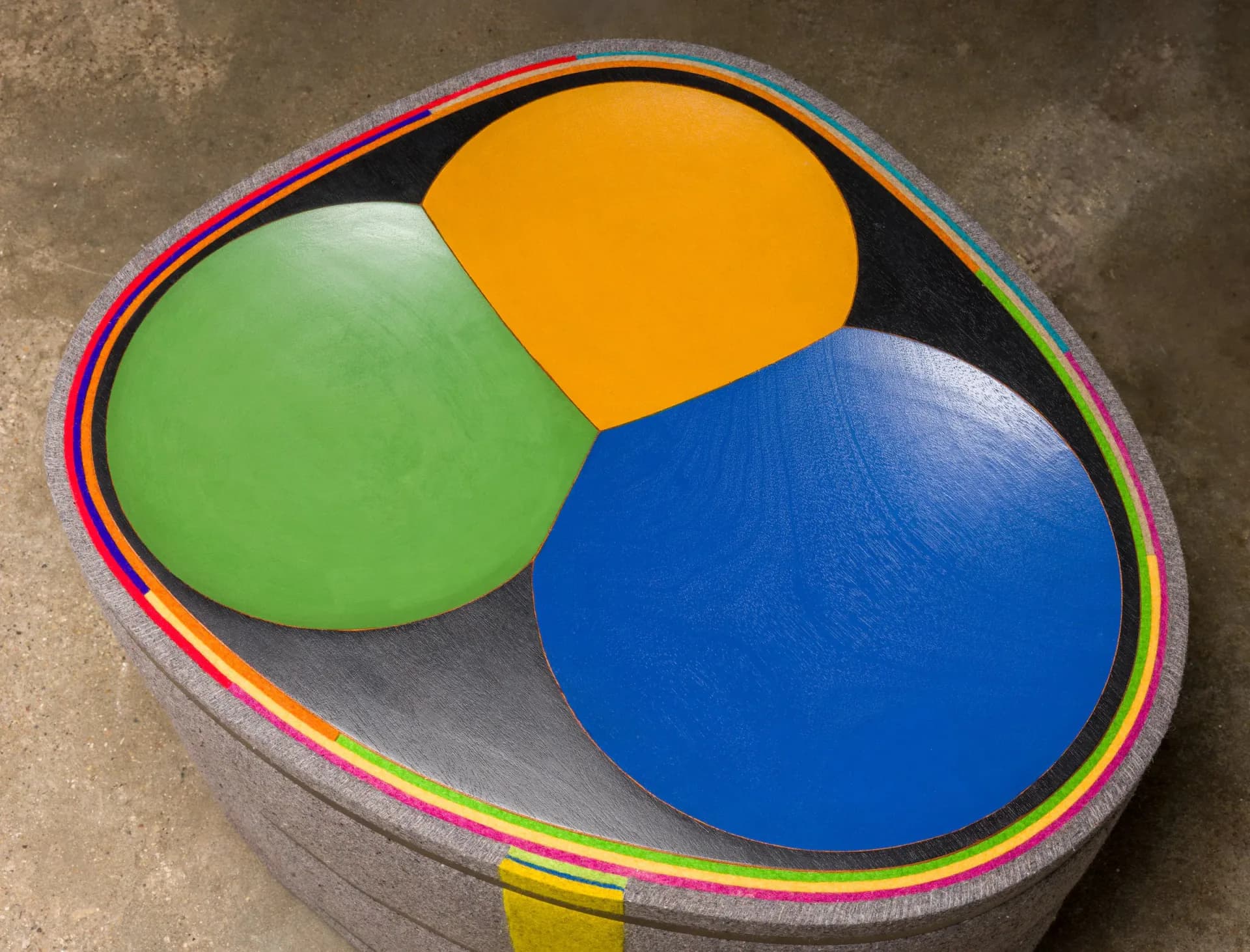 Colorful sculptural bowl with green, orange, and blue sections and a rainbow-striped rim, photographed from above by Tom Loeser.