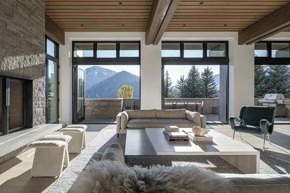 Modern mountain-view living room with floor-to-ceiling windows, neutral furnishings, and contemporary fireplace designed by Tori Catherall.