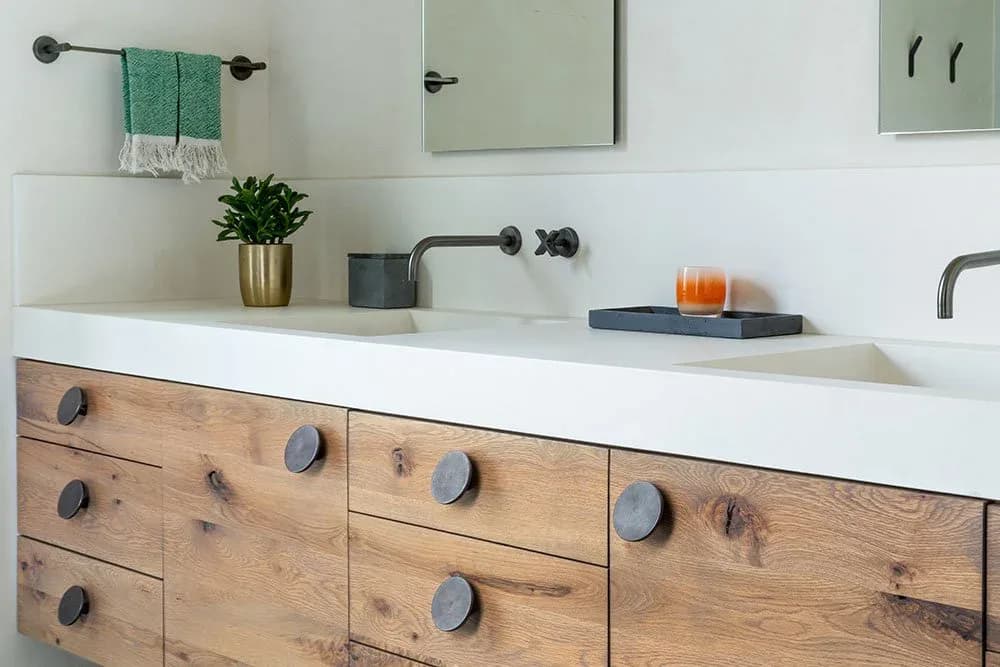 Modern bathroom vanity with natural wood cabinetry, white countertop, dual sinks, and black hardware fixtures, designed by Tori Catherall.