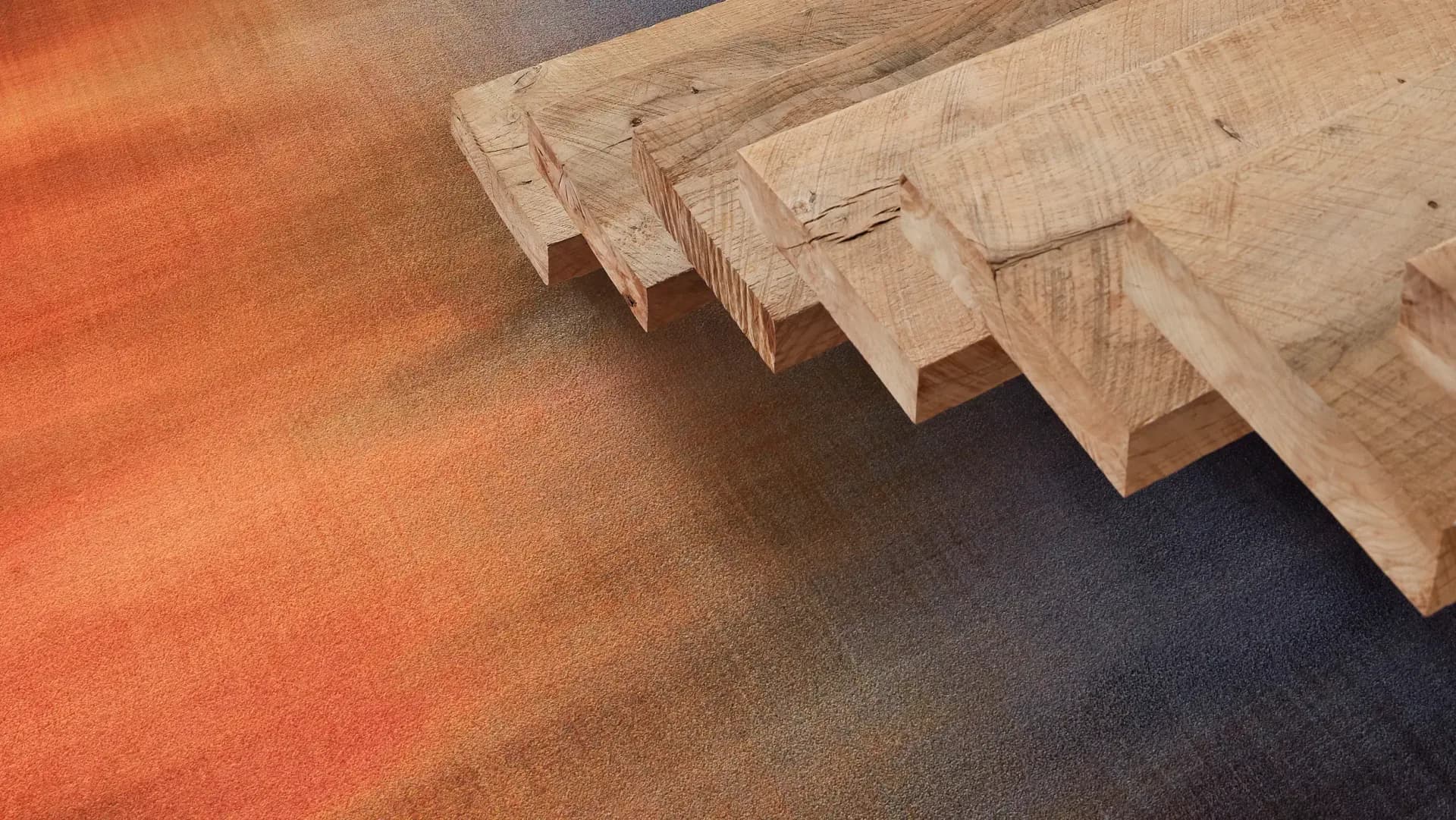 Wooden architectural moldings and trim pieces arranged on a warm orange and charcoal floor surface, showcasing material details and craftsmanship by Tugba Ozkan.