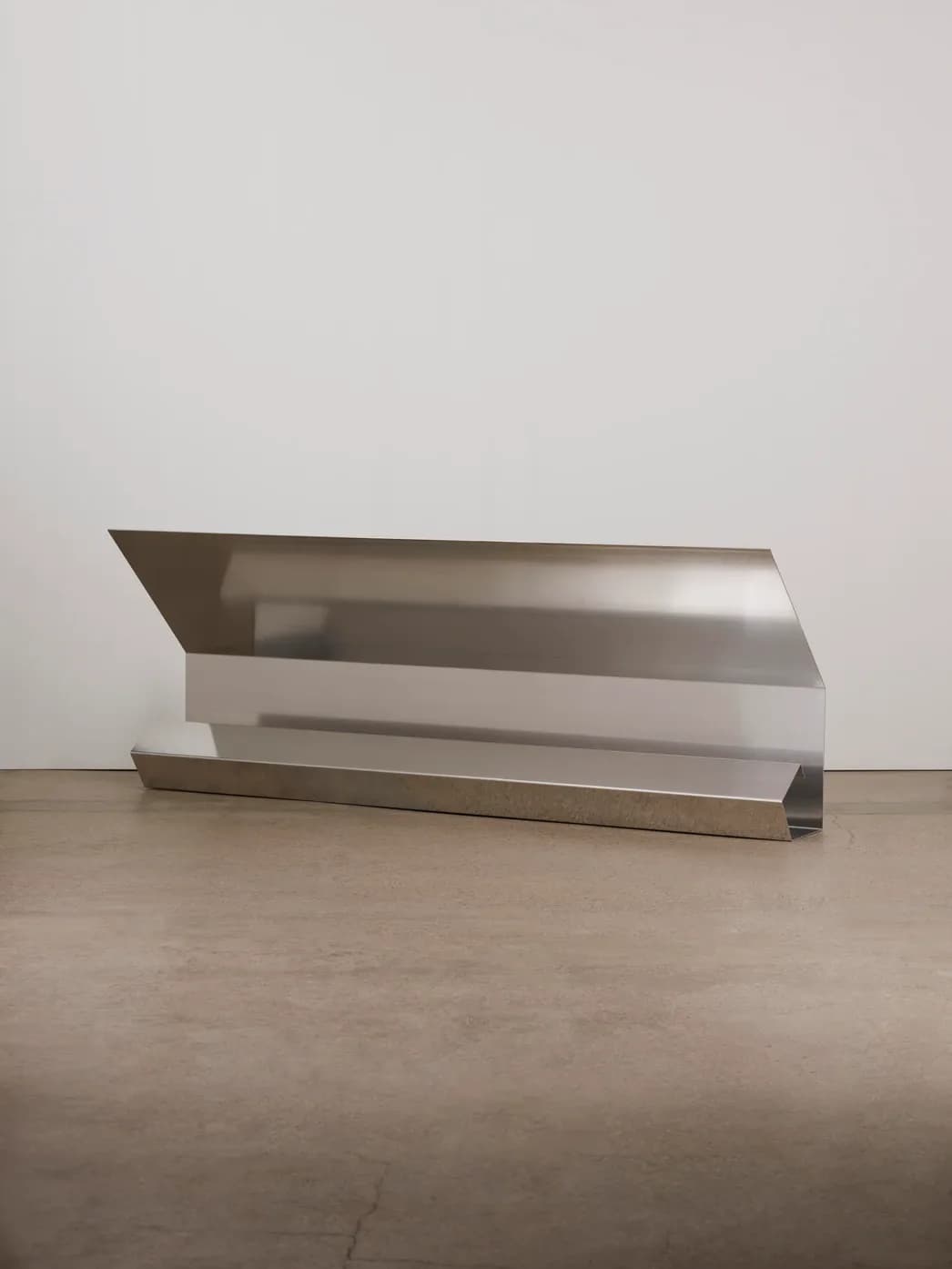 Minimalist stainless steel sculptural furniture piece with angular, layered forms on concrete floor, a contemporary metal installation by Umberto Bellardi Ricci.