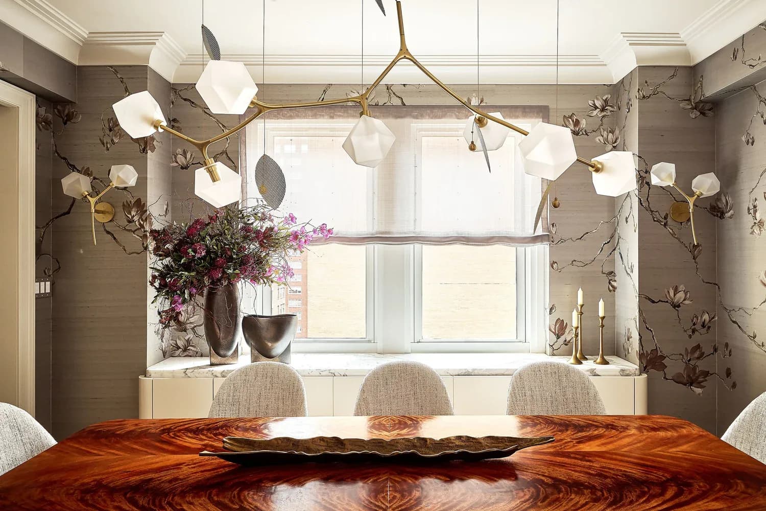 Modern dining room with taupe grasscloth walls, wooden table, pendant lighting, and floral window arrangement by Valerie Goldin-Remm.