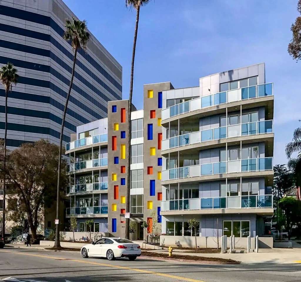 Colorful residential building facade with vibrant blue, red, and yellow vertical panels, balconies, and modern glazing by Valerie Schweitzer.