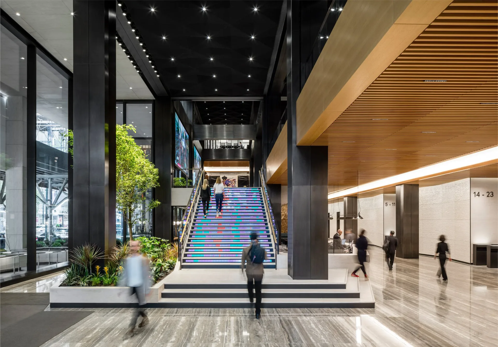 Modern commercial lobby with LED-lit staircase, planted greenery, polished floors, and minimalist aesthetic by Vané Broussard.