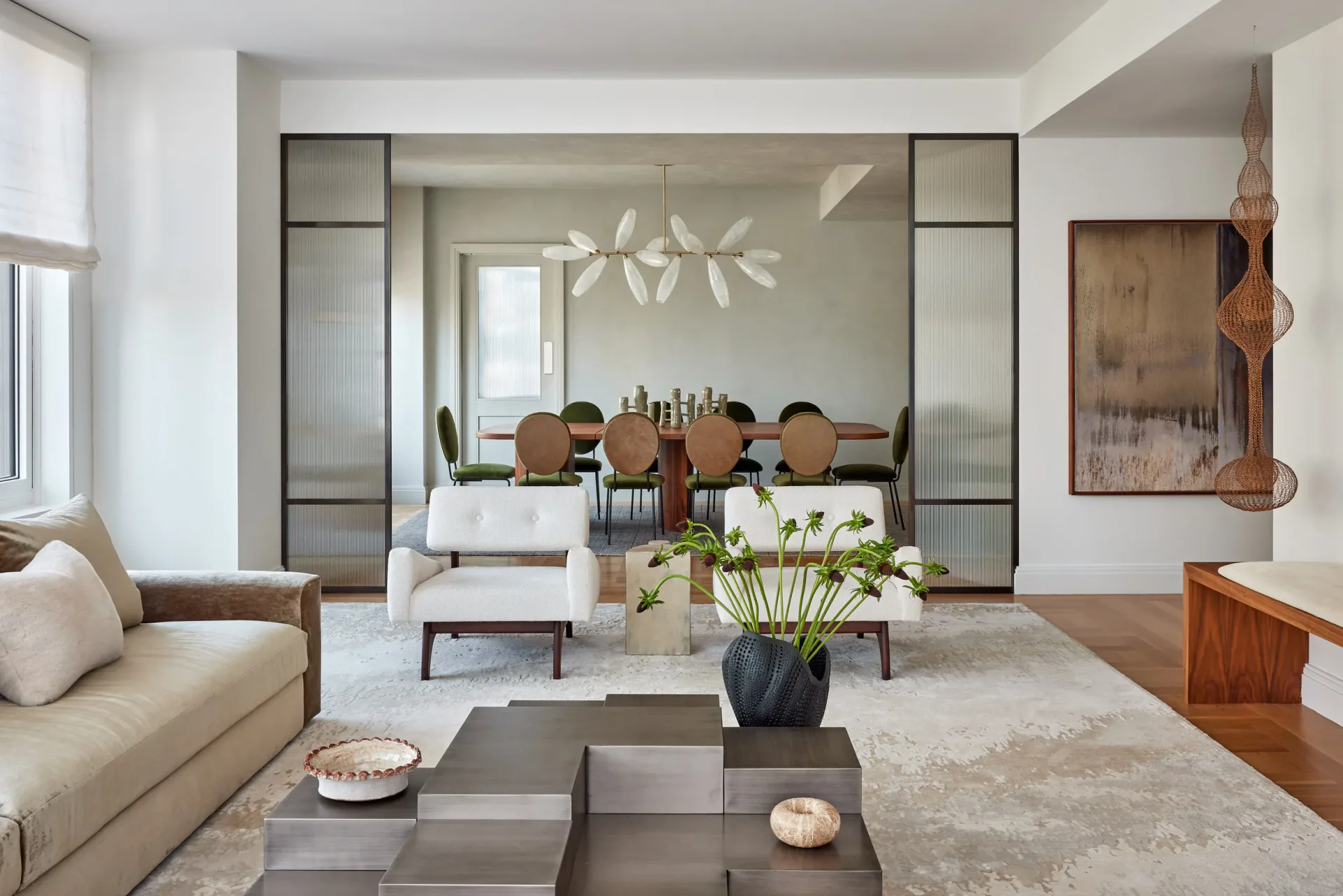 Modern living room with cream sofa, geometric area rug, and glass-paneled doors opening to dining area, designed by Vanessa Rome.