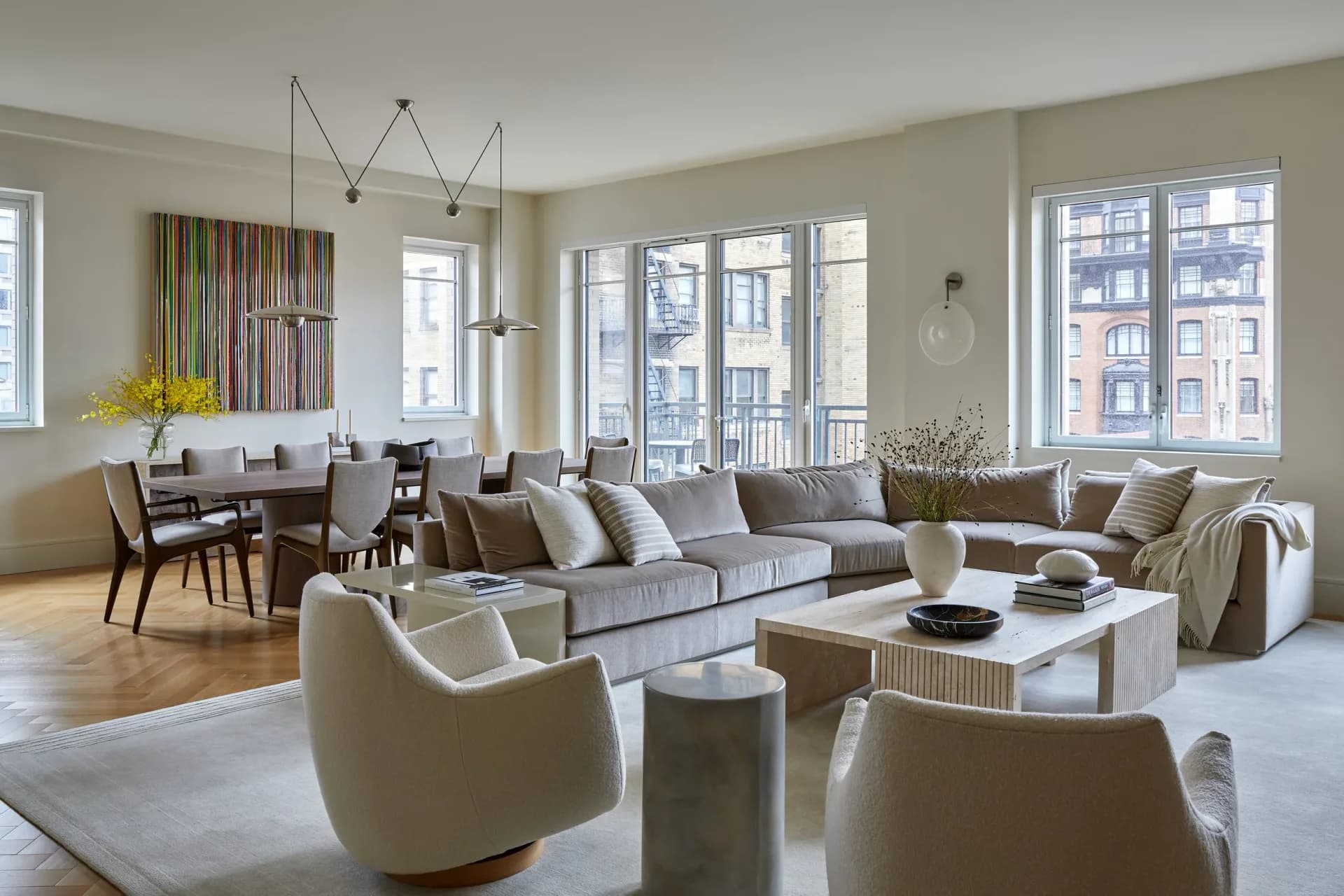 Bright contemporary living room with neutral palette features gray sectional, cream swivel chairs, white coffee table, and expansive windows overlooking cityscape by Vanessa Rome.