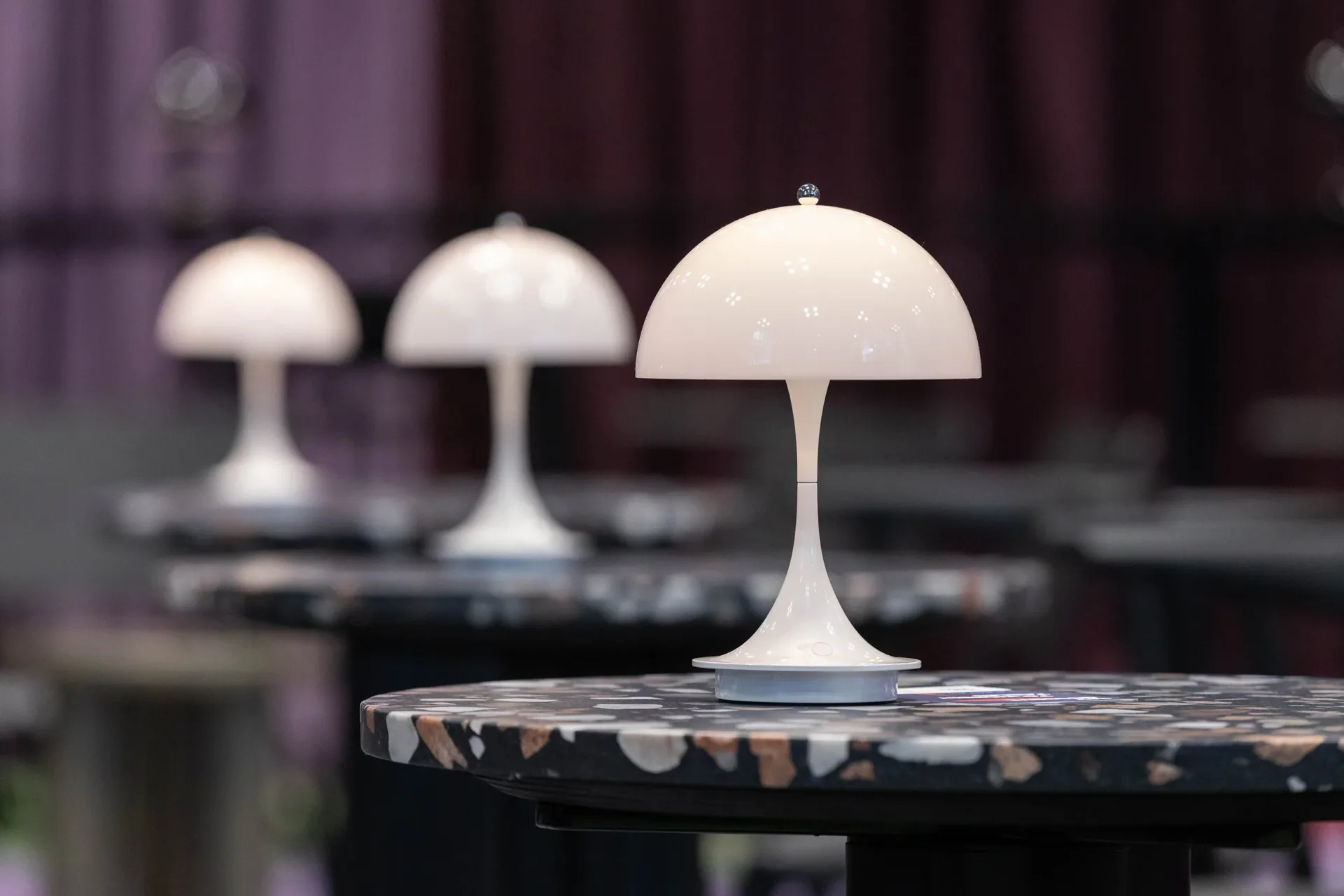 Three white mushroom-shaped table lamps with dome tops displayed on dark surfaces, showcasing mid-century modern lighting design by Vanessa Watts.