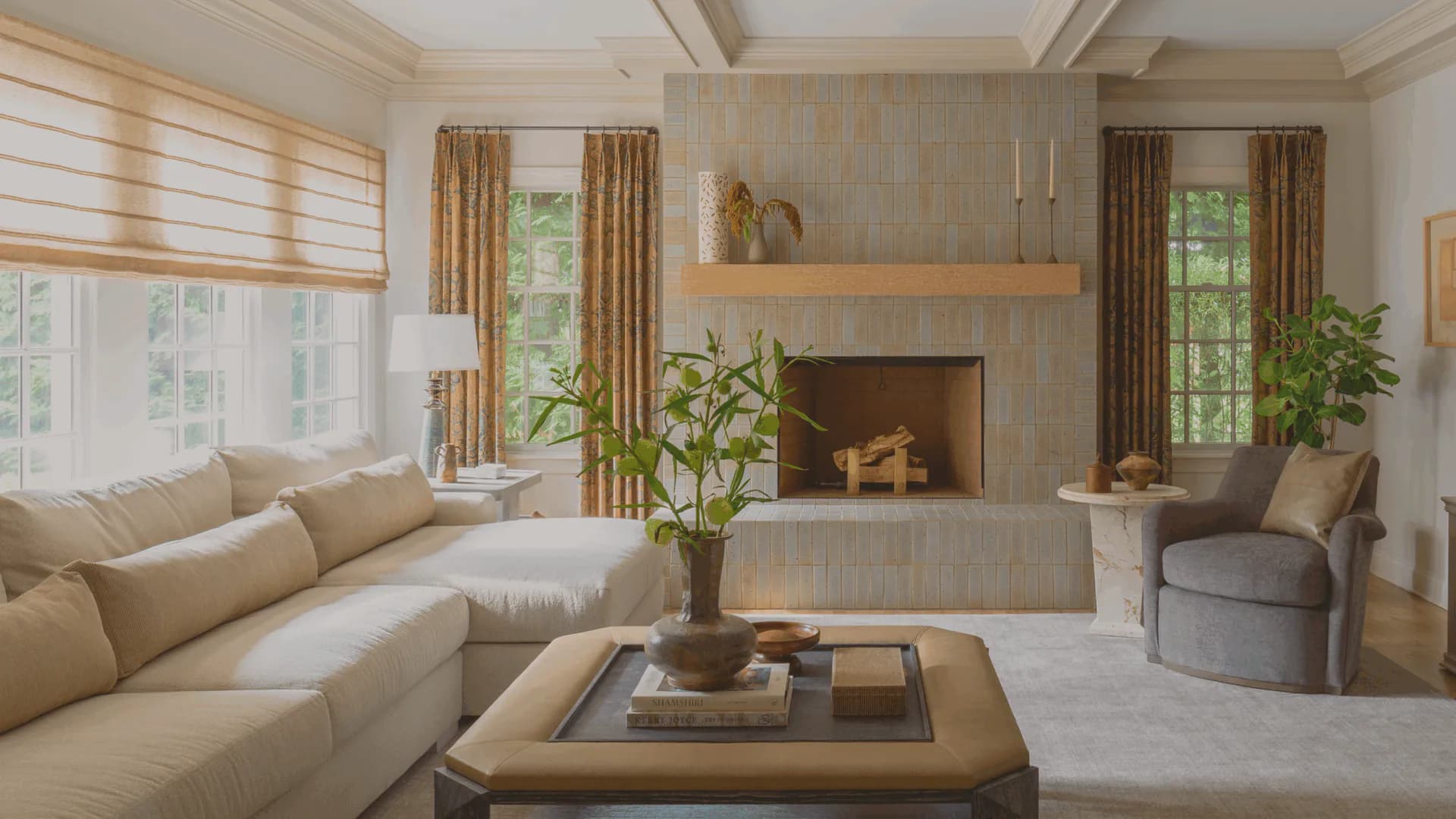 Elegant living room with cream sectional sofa, fireplace with wooden mantel, coffered ceiling, warm neutral palette, and abundant natural light by Victoria Bartholomew.