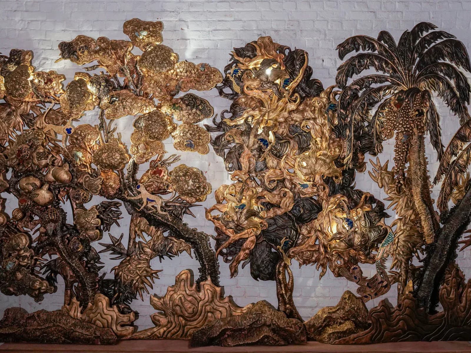 Ornate carved wooden wall installation with gilt detailing and botanical motifs, featuring layered relief panels and decorative foliage elements by Vikram Goyal.