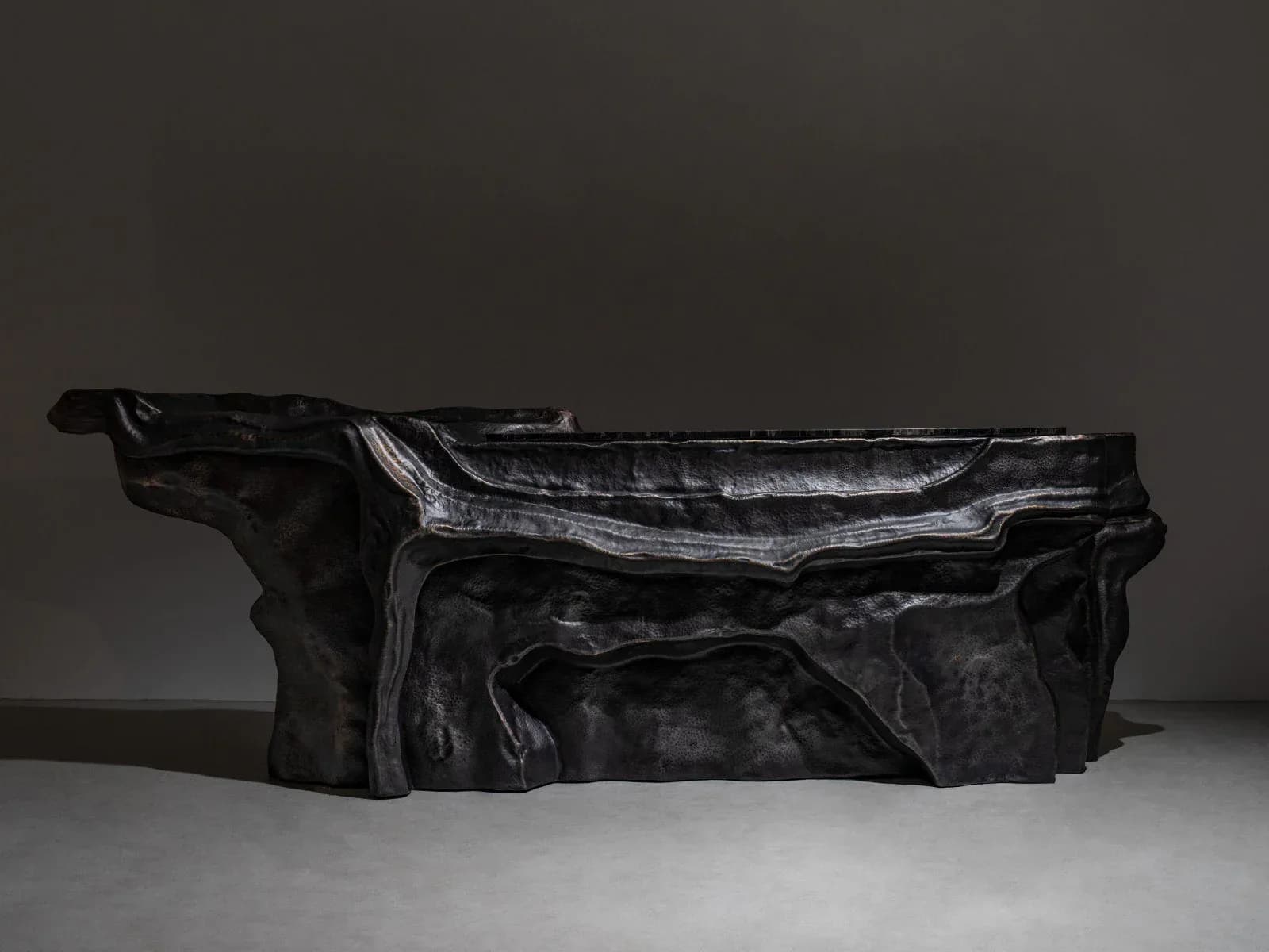 A sculptural black furniture piece with dramatic angular forms and textured surfaces against a neutral background by Vikram Goyal.
