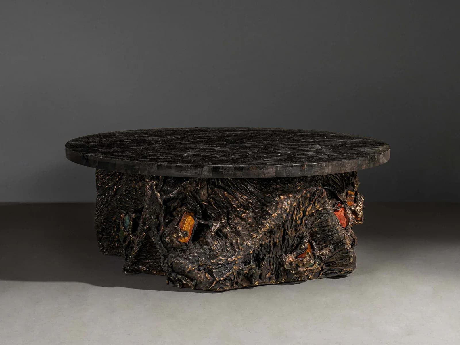 A sculptural table with a dark textured bark-like base and smooth dark top surface, showcasing organic materials and craftsmanship by Vikram Goyal.