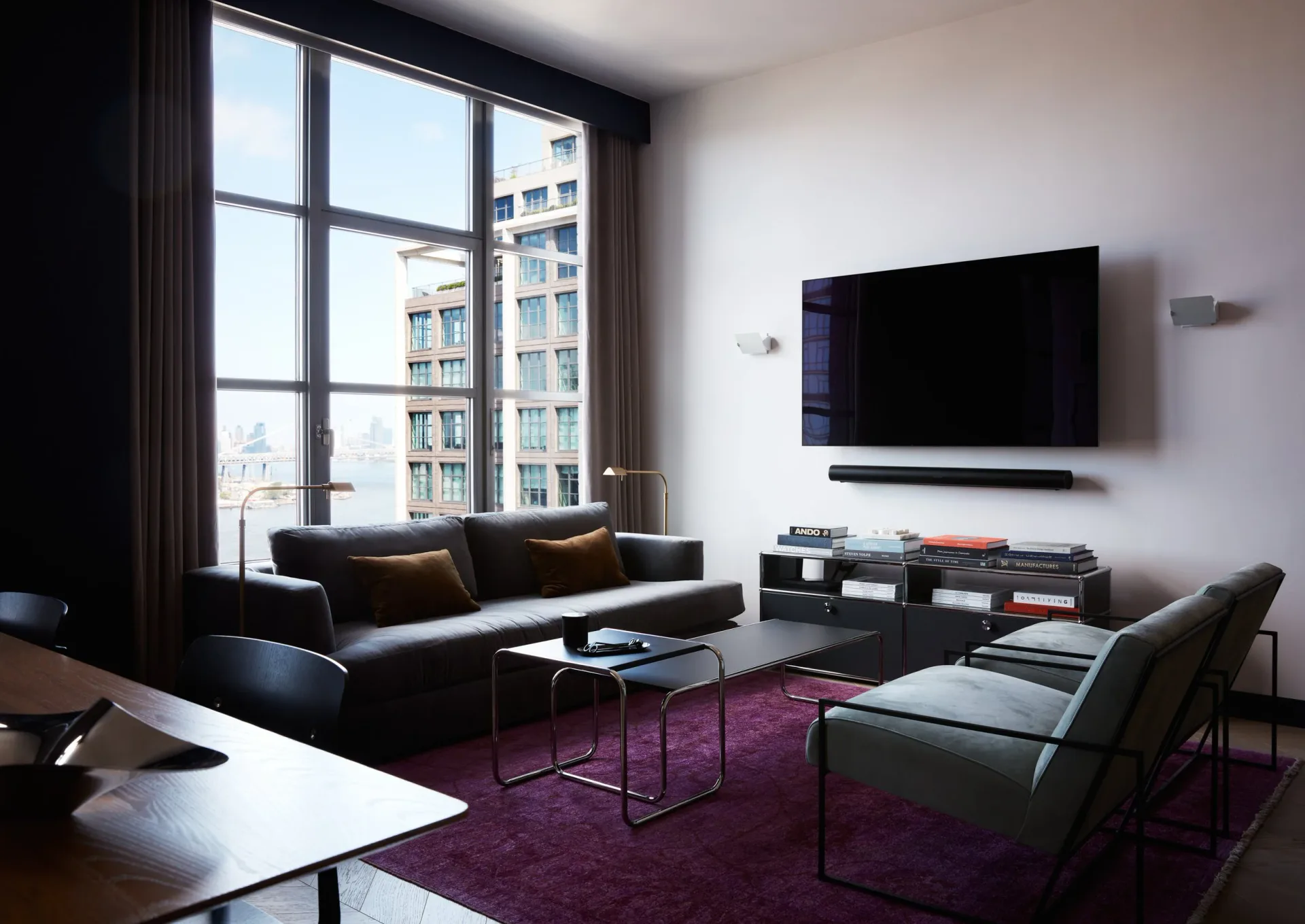 Modern living room with black sofa, purple area rug, floor-to-ceiling windows, wall-mounted TV, and minimalist furnishings by Vinh Nguyen.