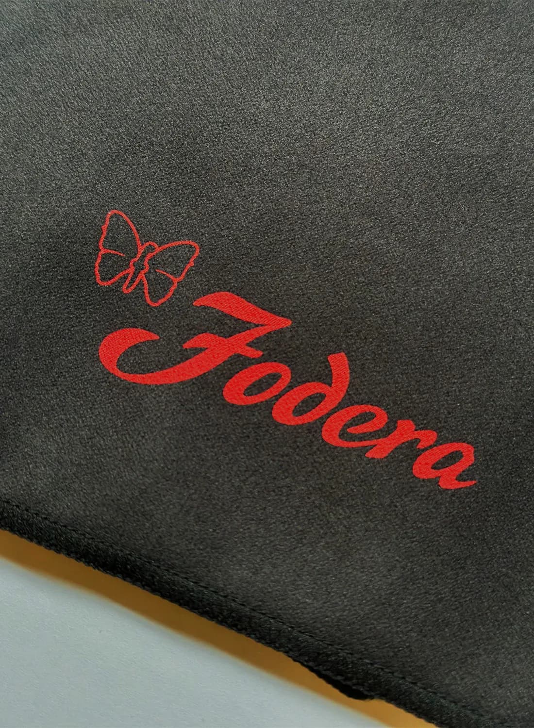 Red embroidered butterfly and script logo on charcoal fabric garment, branding detail by Vinny Fodera.