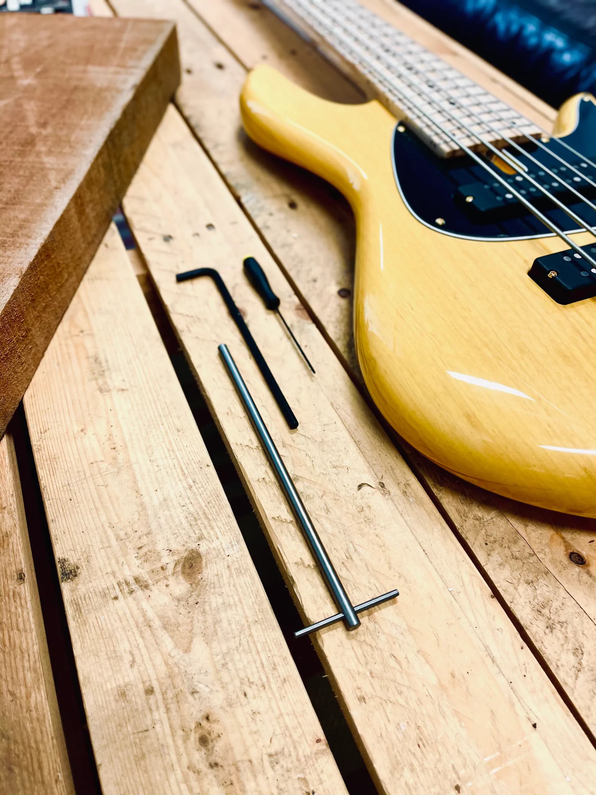 Yellow electric guitar with black pickguard rests on wooden workbench next to design sketches and tools by Vinny Fodera.