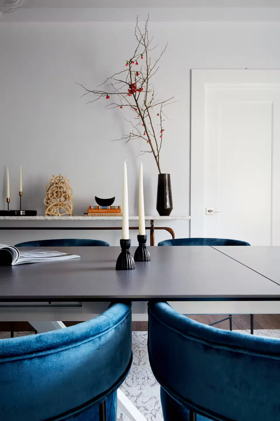Modern dining room with black table, blue velvet chairs, fireplace mantel with candles and botanical branch arrangement by Vivian Bayles.