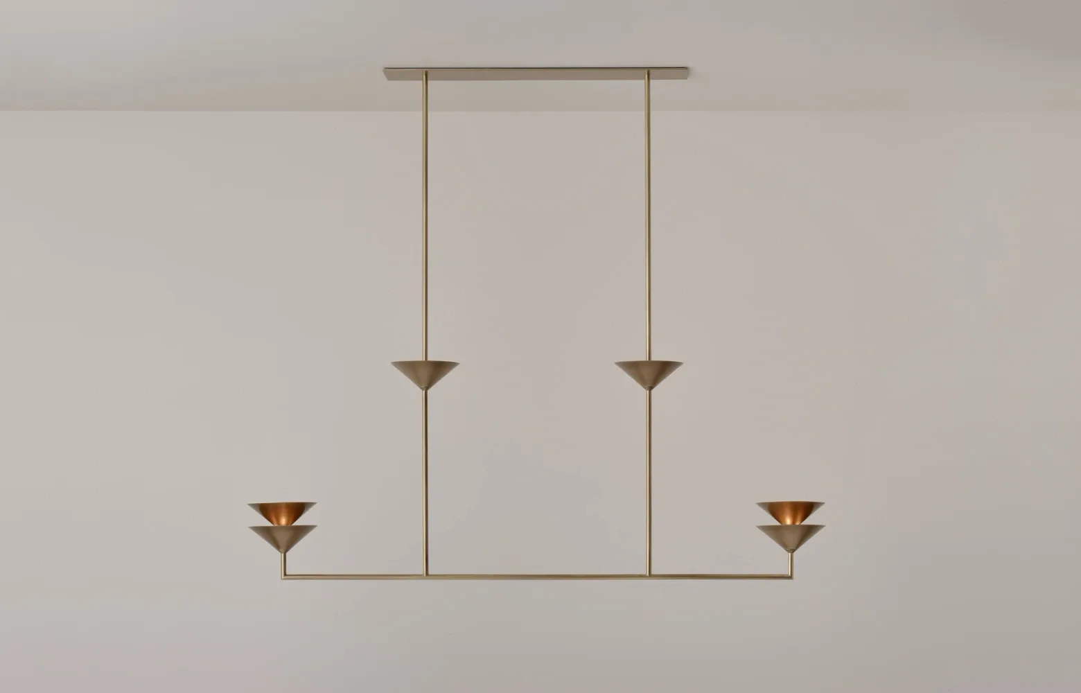 Minimalist lighting fixture design with vertical brass rods suspended from a horizontal rail, featuring four conical pendant elements arranged symmetrically by Volker Haug.