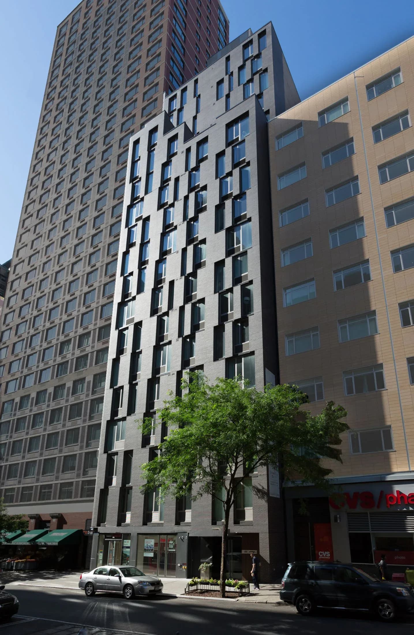 Modern white and black residential building with stacked window pattern nestled between taller structures on an urban street, designed by Weilin Berkey.