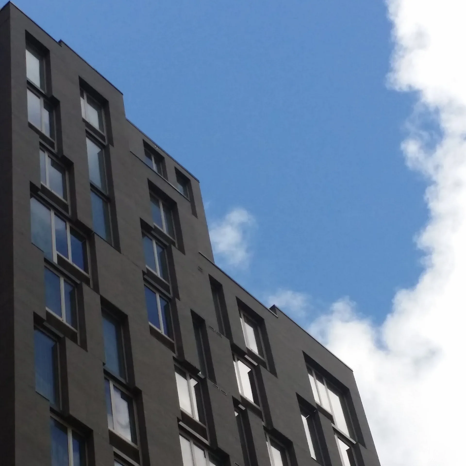 Modern residential building facade with dark gray cladding and geometric window patterns against a blue sky, designed by Weilin Berkey.