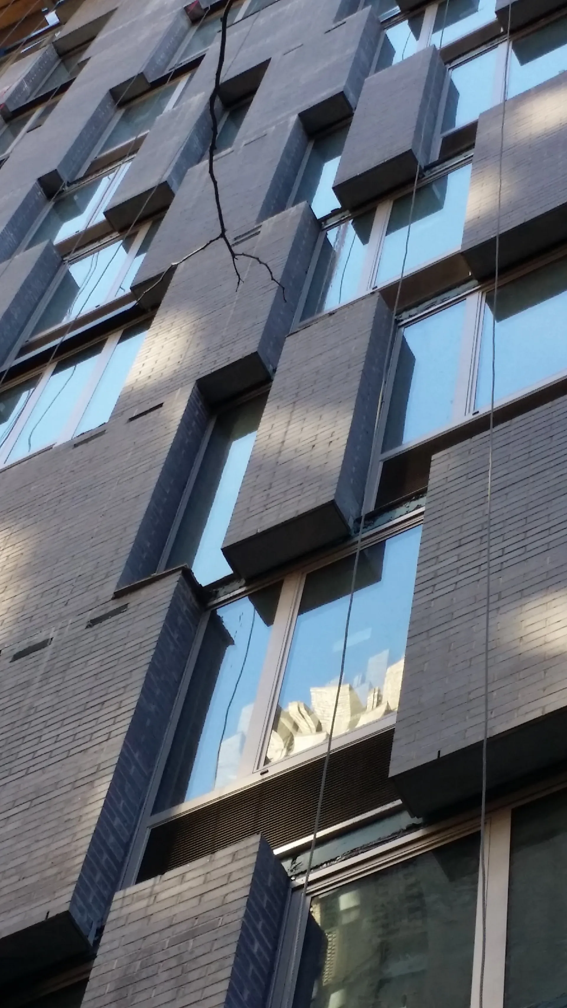 Modern residential building facade with stacked brick and glass windows, geometric black sunshade elements, and exposed utility cables, architectural design by Weilin Berkey.