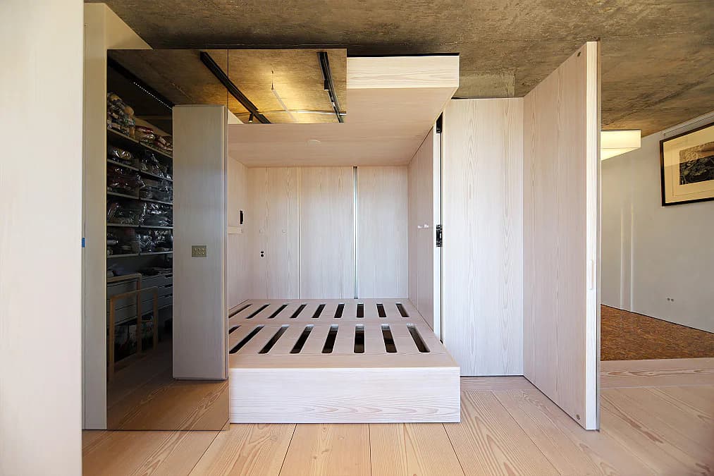 Modern bedroom with white built-in cabinetry, striped bed frame, concrete ceiling, and minimalist aesthetic by Wes Rozen.