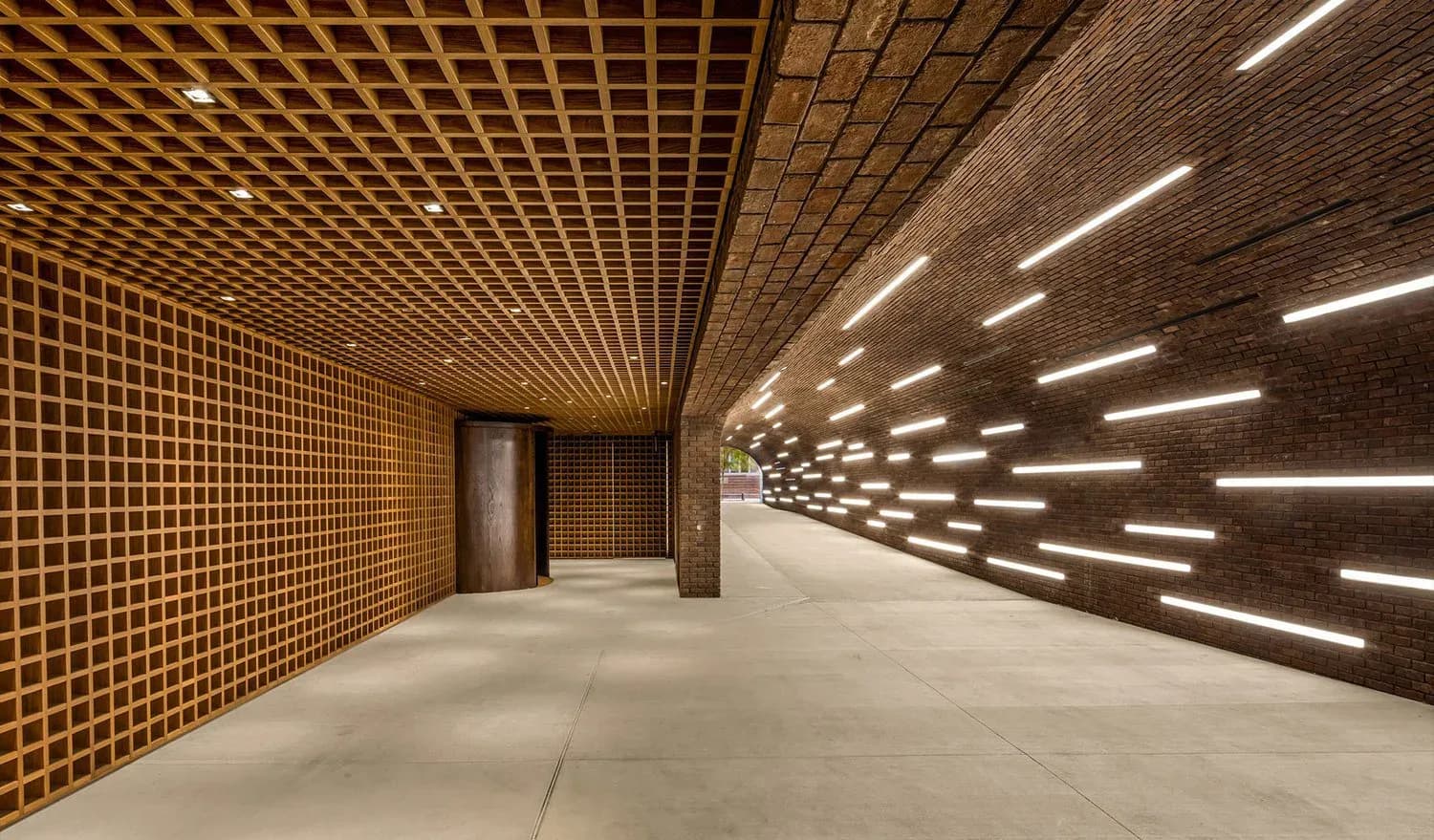 Modern corridor with geometric wood lattice walls, linear ceiling lights, and polished concrete floors, designed by William Armstrong.