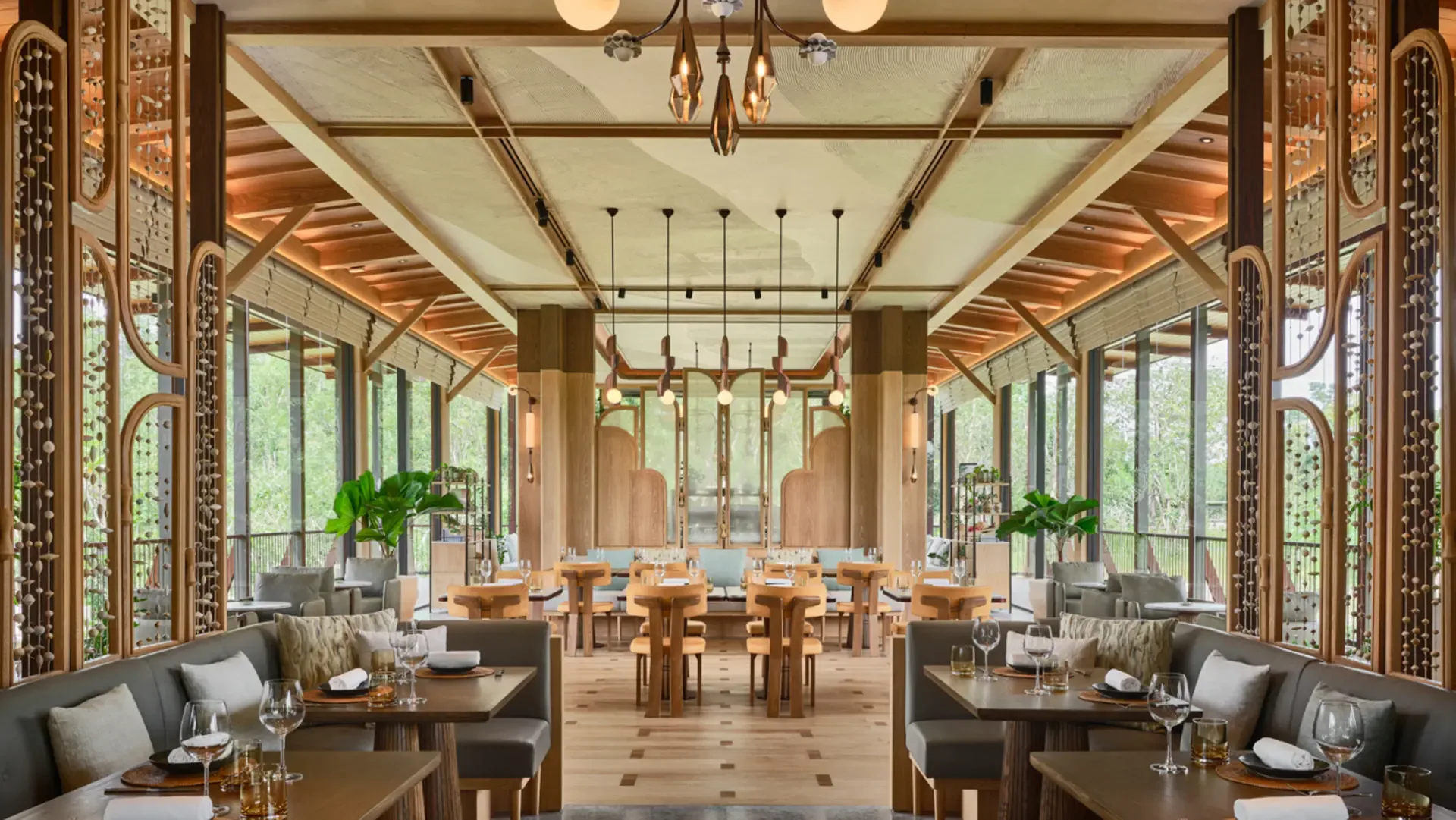 Luxurious dining pavilion with symmetrical layout, coffered ceiling, brass chandeliers, floor-to-ceiling windows, warm wood tones, and potted plants by William Harris.