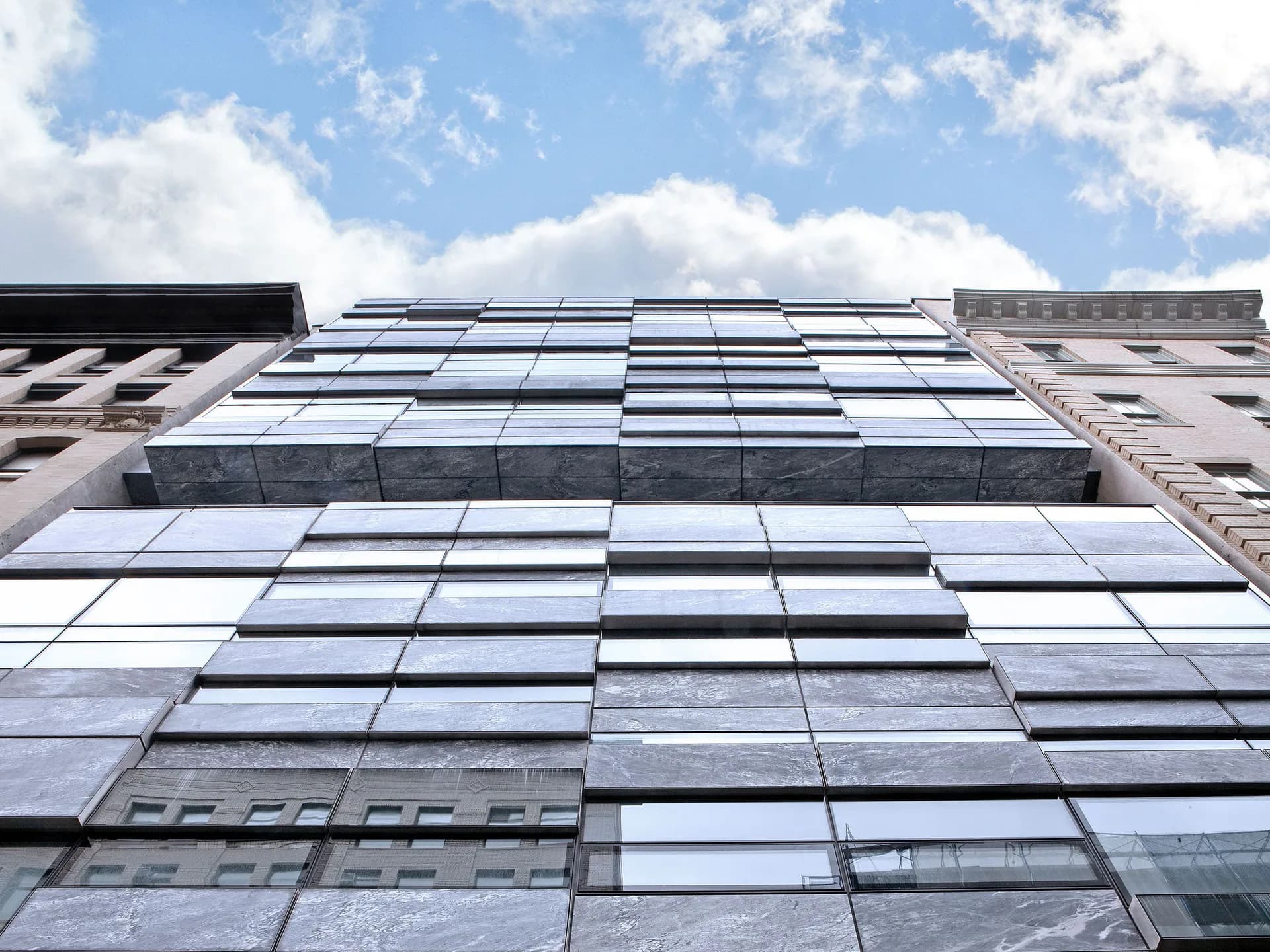 Modern facade with stacked horizontal glass and metal panels photographed from below against a cloudy sky by Winka Dubbeldam.