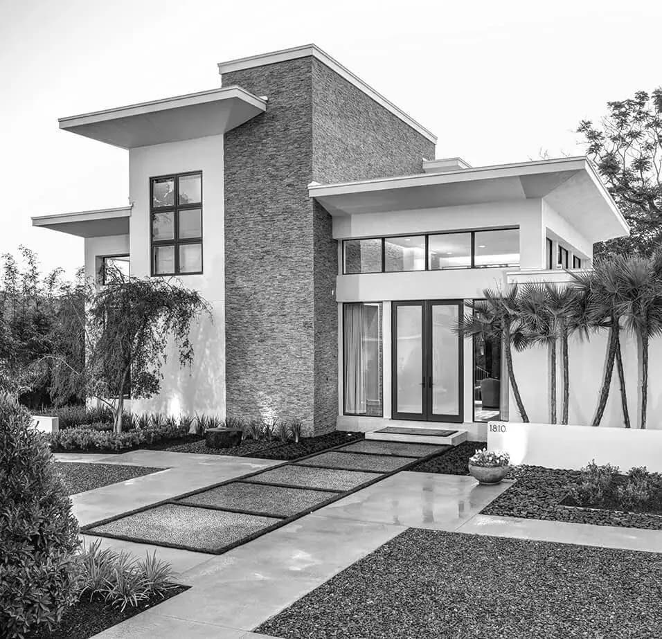 Modern two-story residential home with stone and white facade, flat roof overhangs, large windows, and minimalist landscaping by Yaminah Rosa.