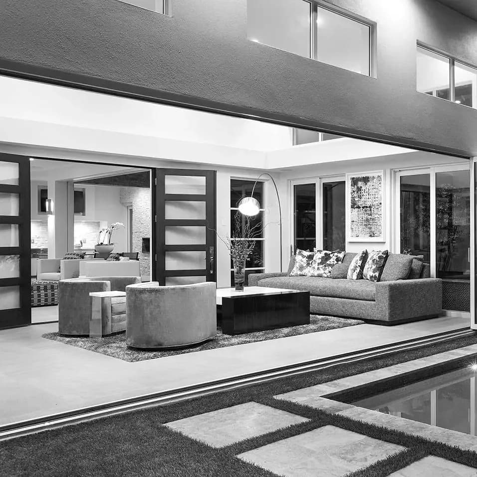 Modern open-plan living space with gray concrete elements, neutral palette, and floor-to-ceiling windows opening to exterior terrace by Yaminah Rosa.