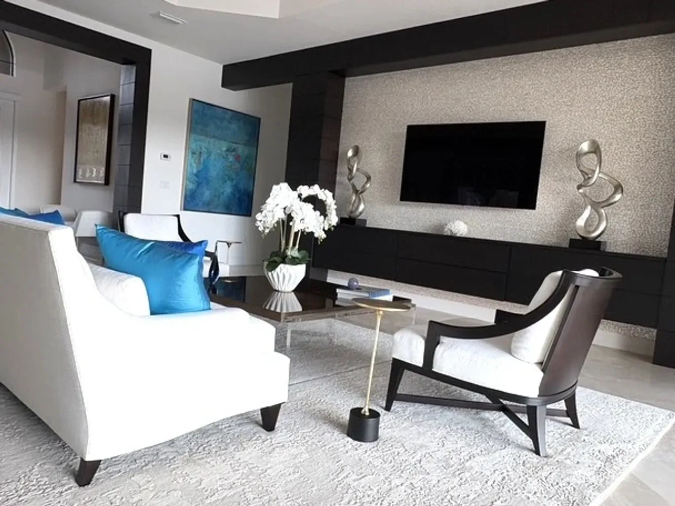 Modern living room with black and white color scheme, blue accent chair, floating entertainment unit, and sculptural décor by Yvonne Compitello.
