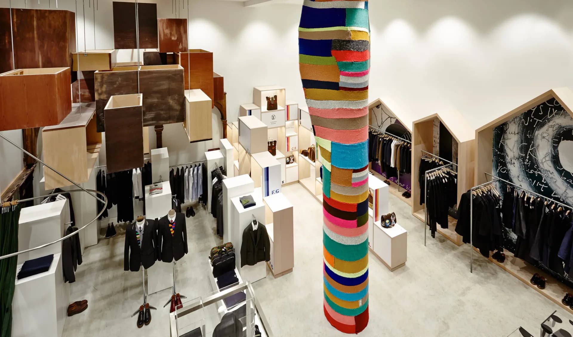 Interior showroom with white flooring, wooden display units, clothing racks, and a striking central column wrapped in colorful rainbow-striped fabric by Zachary Lewis.