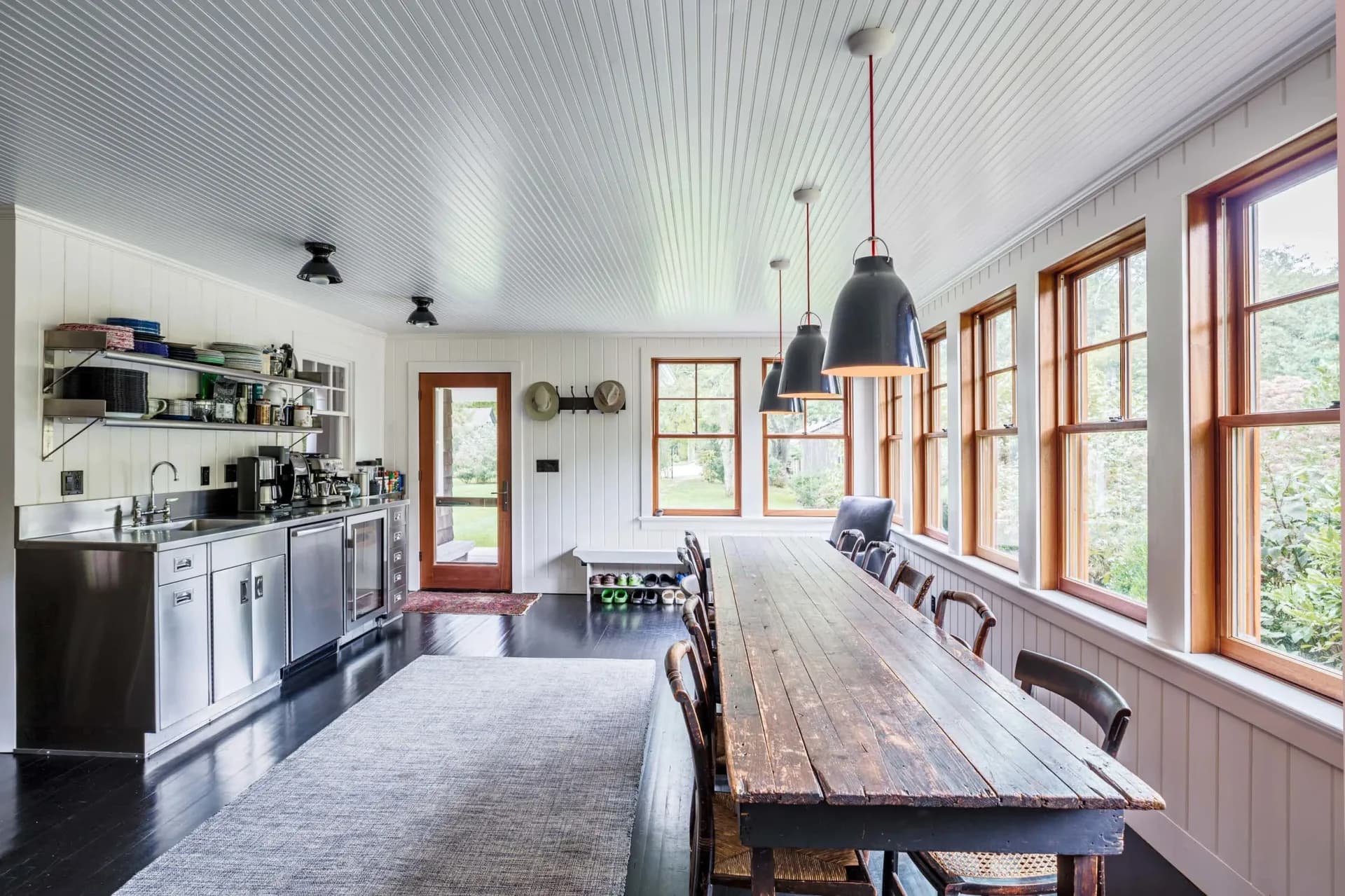 Modern farmhouse kitchen with white cabinetry, wood-framed windows, long dining table, and industrial pendant lights by Zachary Lewis.