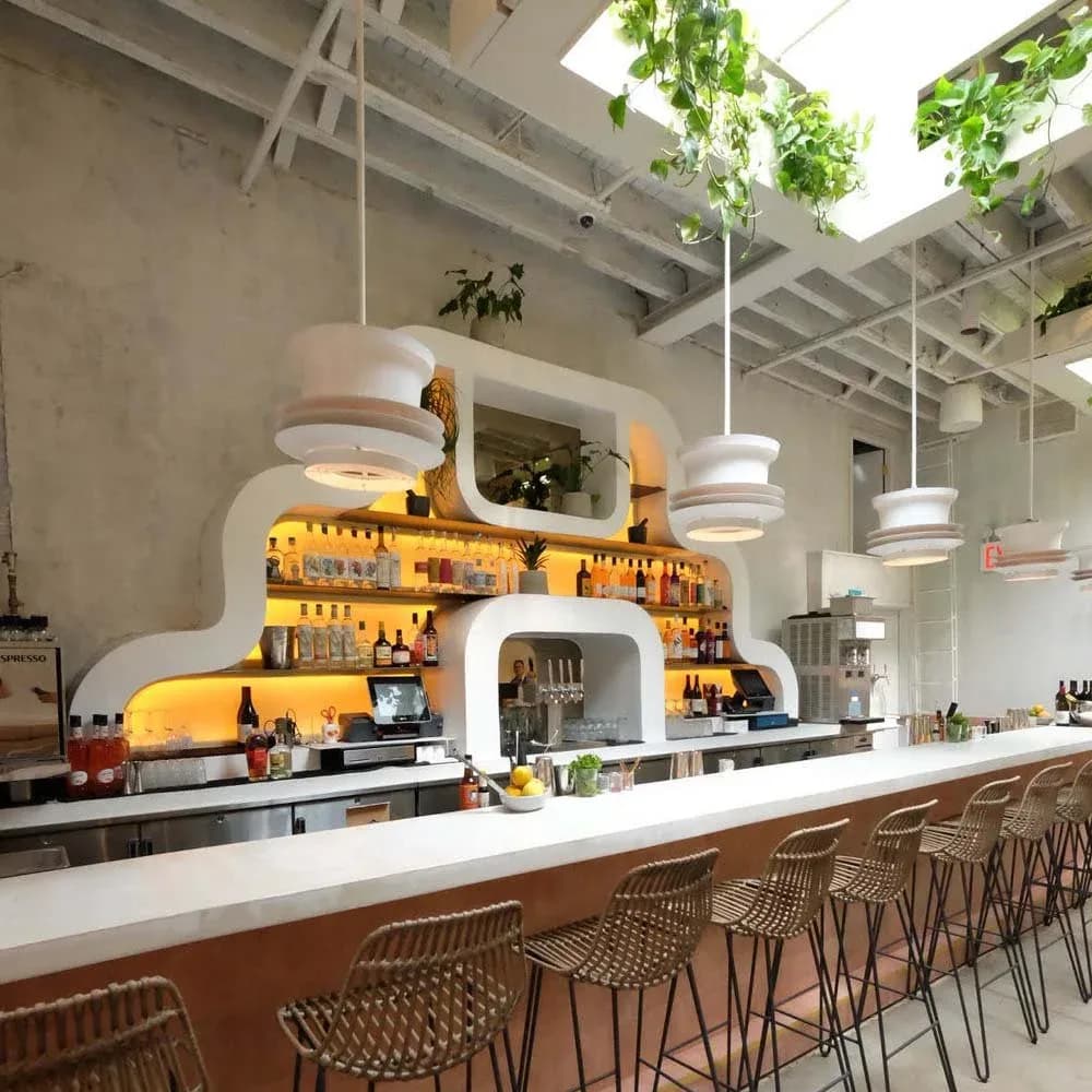 Modern restaurant bar featuring warm yellow-gold shelving, white pendant lighting, concrete walls, and natural wood seating by Zachary Lewis.
