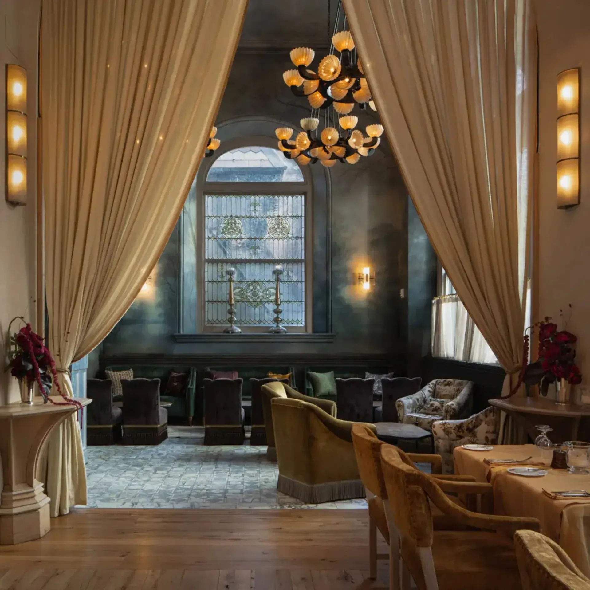 Luxury lounge with cream curtains, black walls, golden pendant lighting, and warm wood furnishings by Zak Profera.
