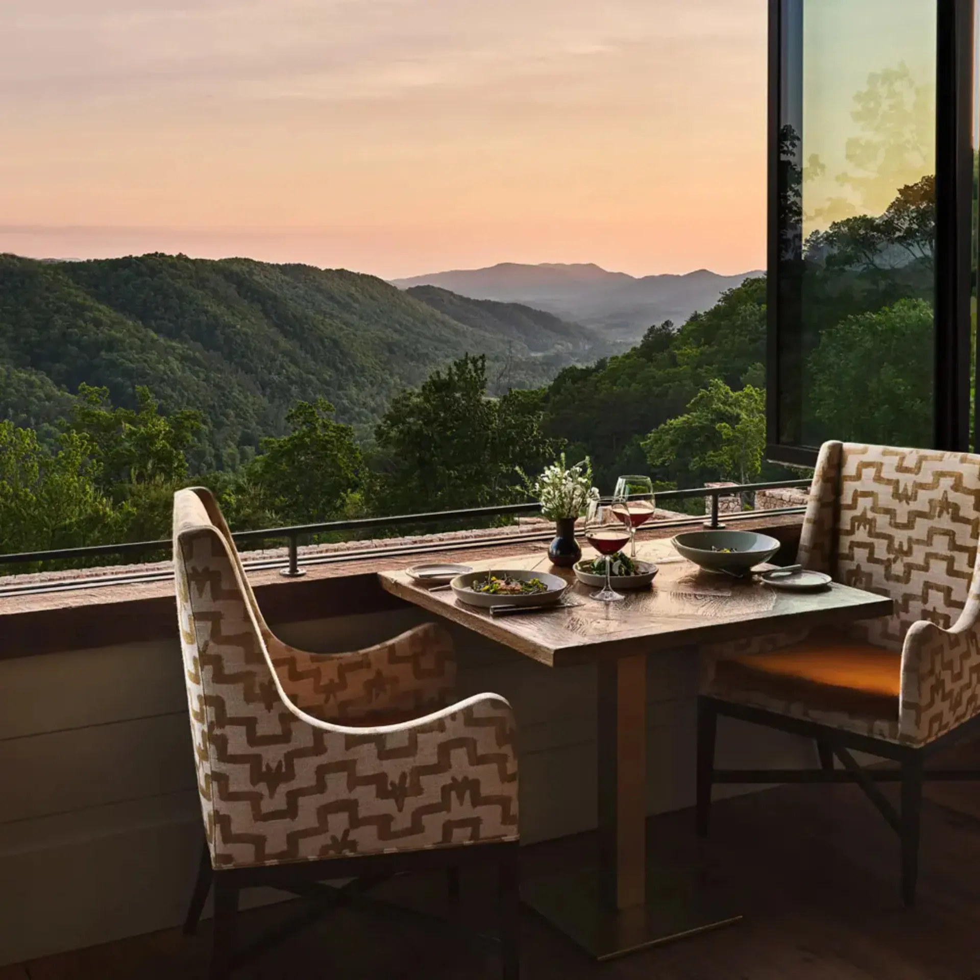 Modern dining space with patterned chairs overlooking mountainous valley landscape at sunset, designed by Zak Profera.