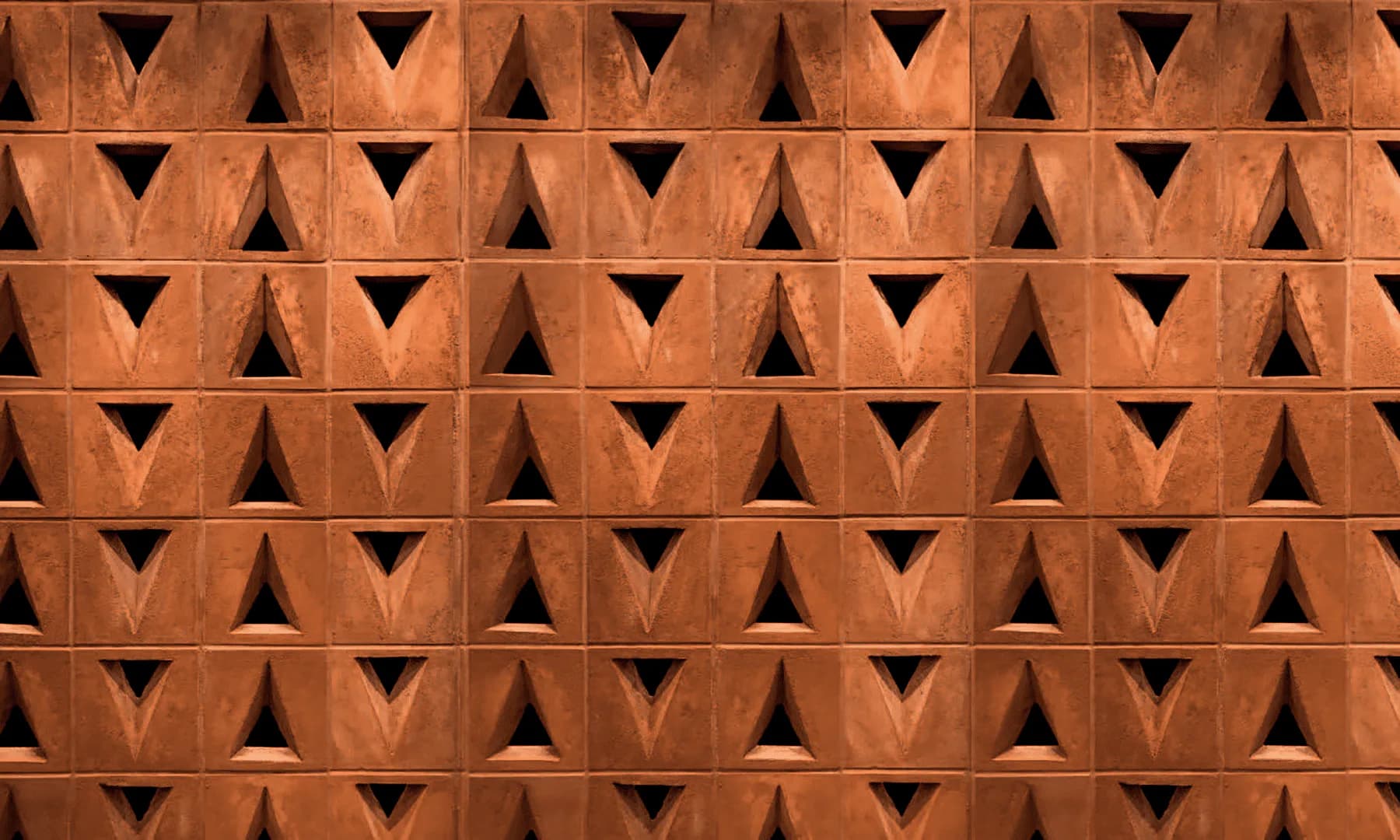 Terracotta brick wall with repeating triangular relief pattern creating dynamic shadow play, architectural detail by Zanini de Zanine Caldas.