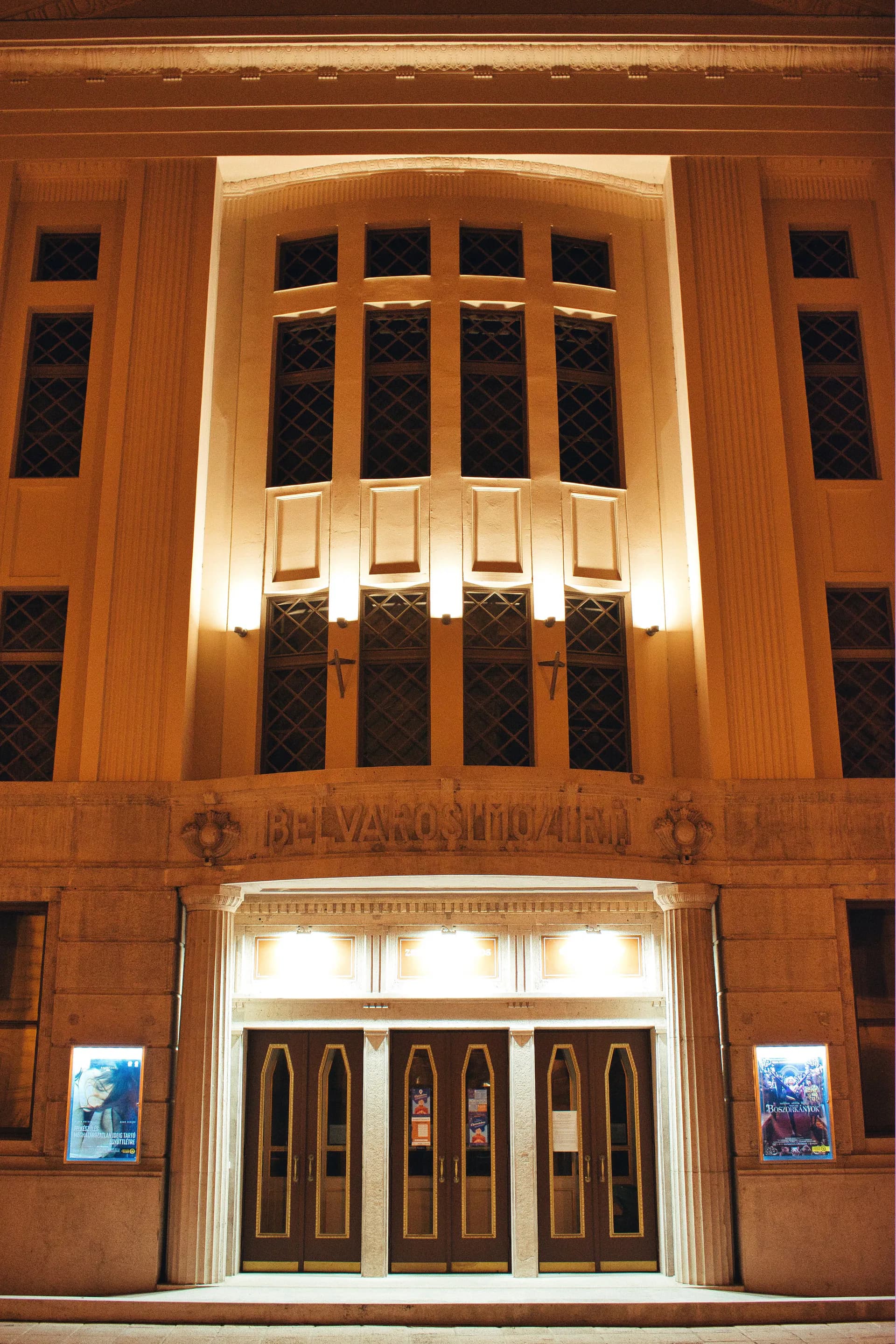 Art Deco theater facade with warm wood paneling, illuminated arched window with geometric patterned glass, and bronze doors, designed by Zaur Gurbanaliyev.