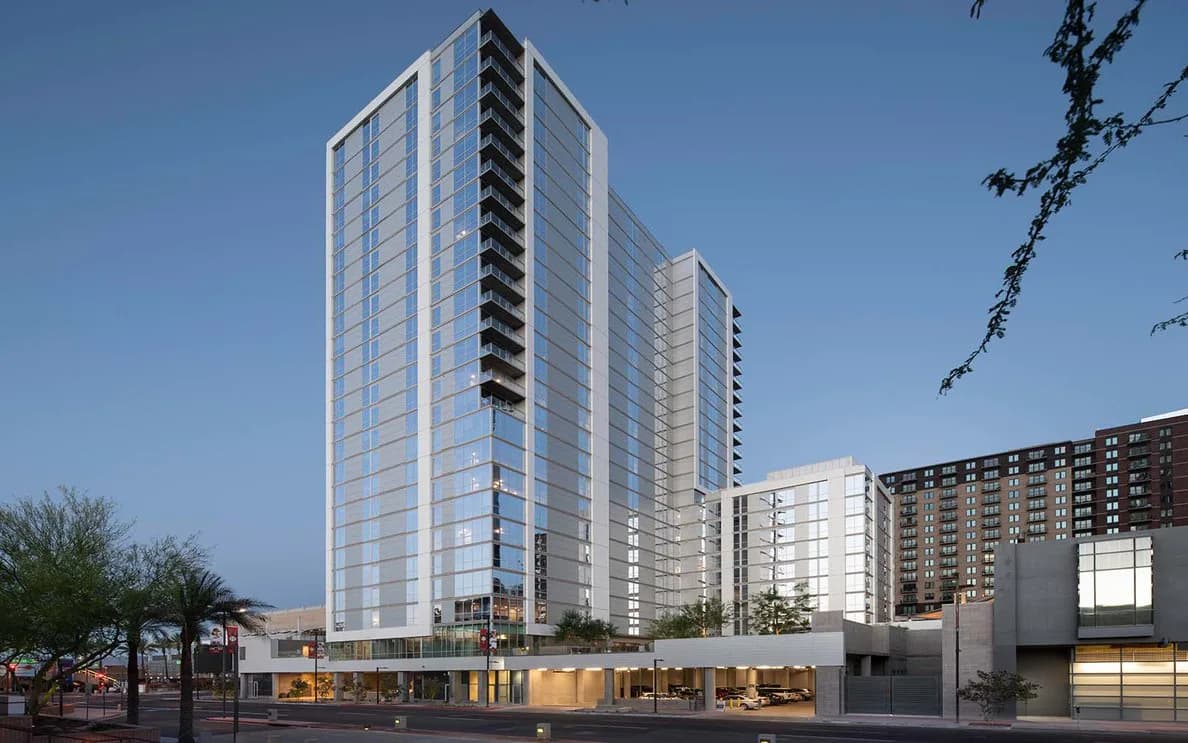 Modern residential tower with stepped glass facade and ground-level retail, rendered in daylight with clear blue sky by Zaur Gurbanaliyev.