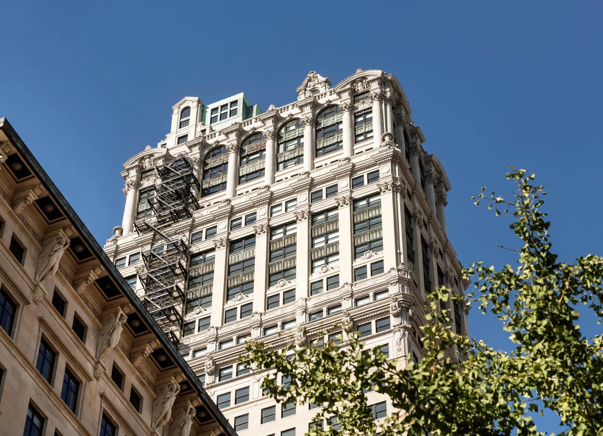 Art Deco skyscraper facade with ornamental limestone detailing, arched windows, and decorative roofline set against clear blue sky by Zaur Gurbanaliyev.
